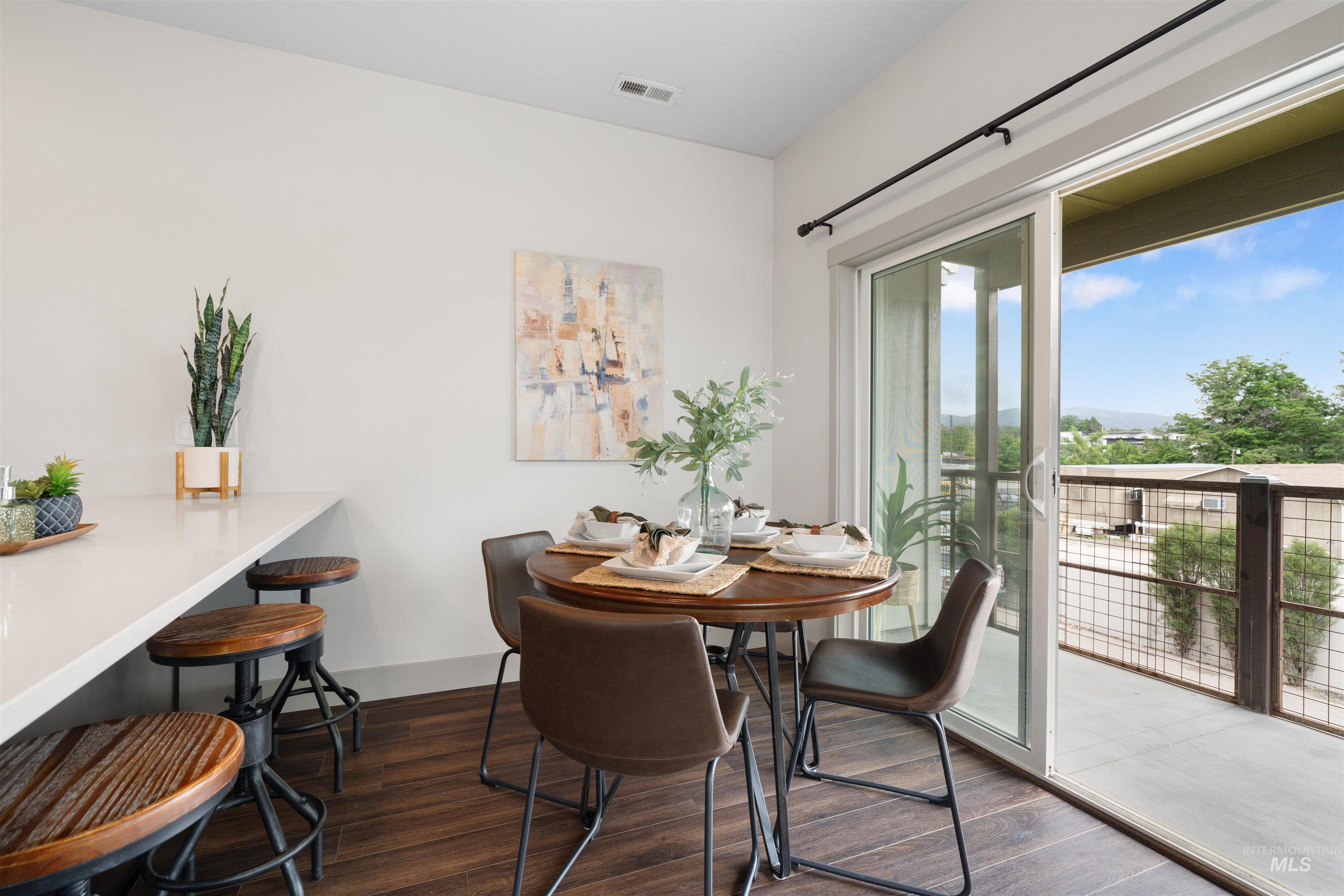 Dining area featuring wood-finish flooring, a white countertop with bar seating, and a sliding glass door providing access to an outdoor balcony with metal railing