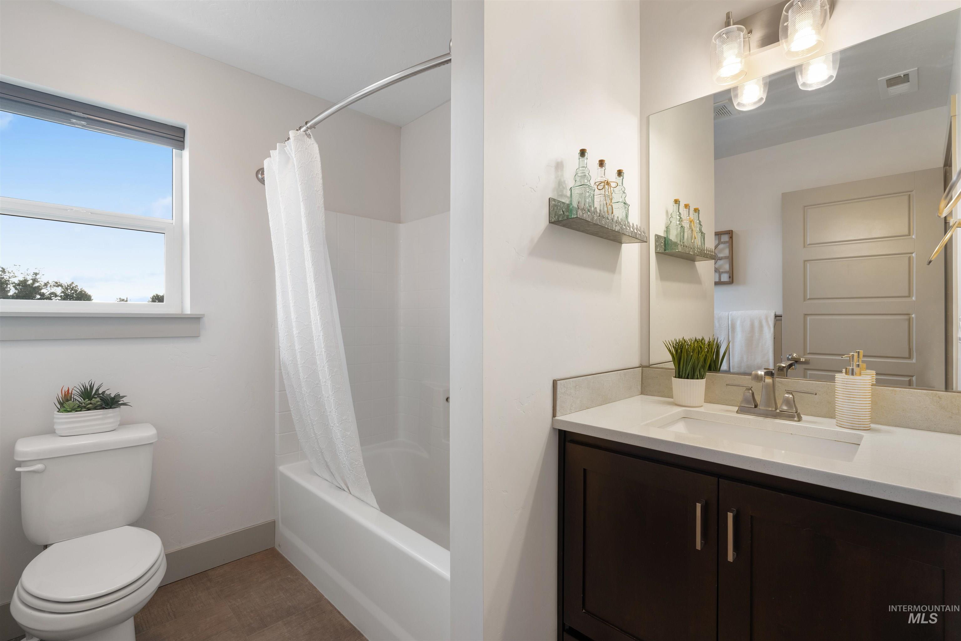 Bathroom featuring a dark wood vanity with a white countertop and integrated sink, a large wall-mounted mirror, a three-light vanity fixture, and a bathtub with a shower