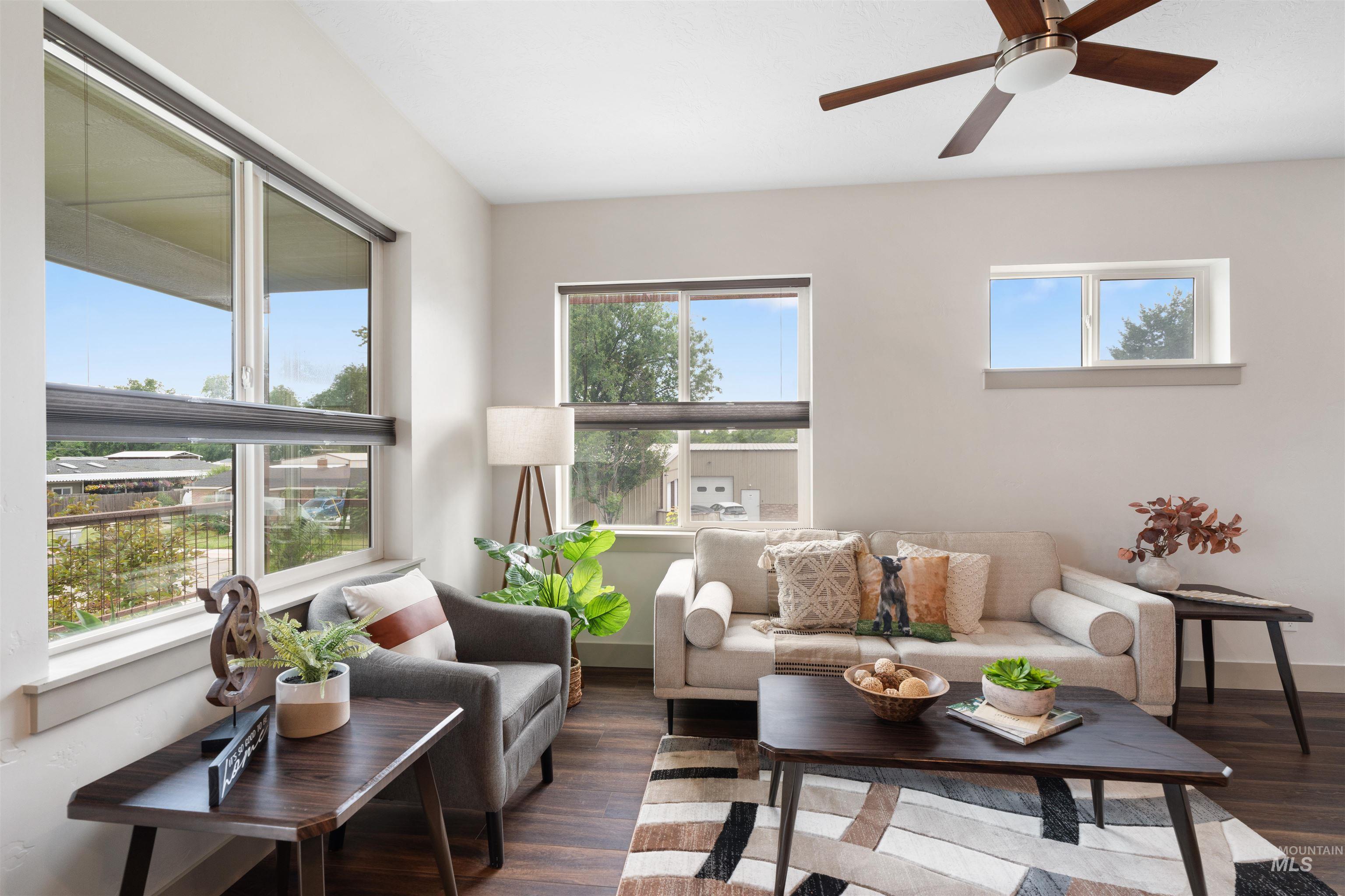 Bright living area featuring wood-finish flooring, multiple windows, a ceiling fan with integrated lighting, and neutral wall tones