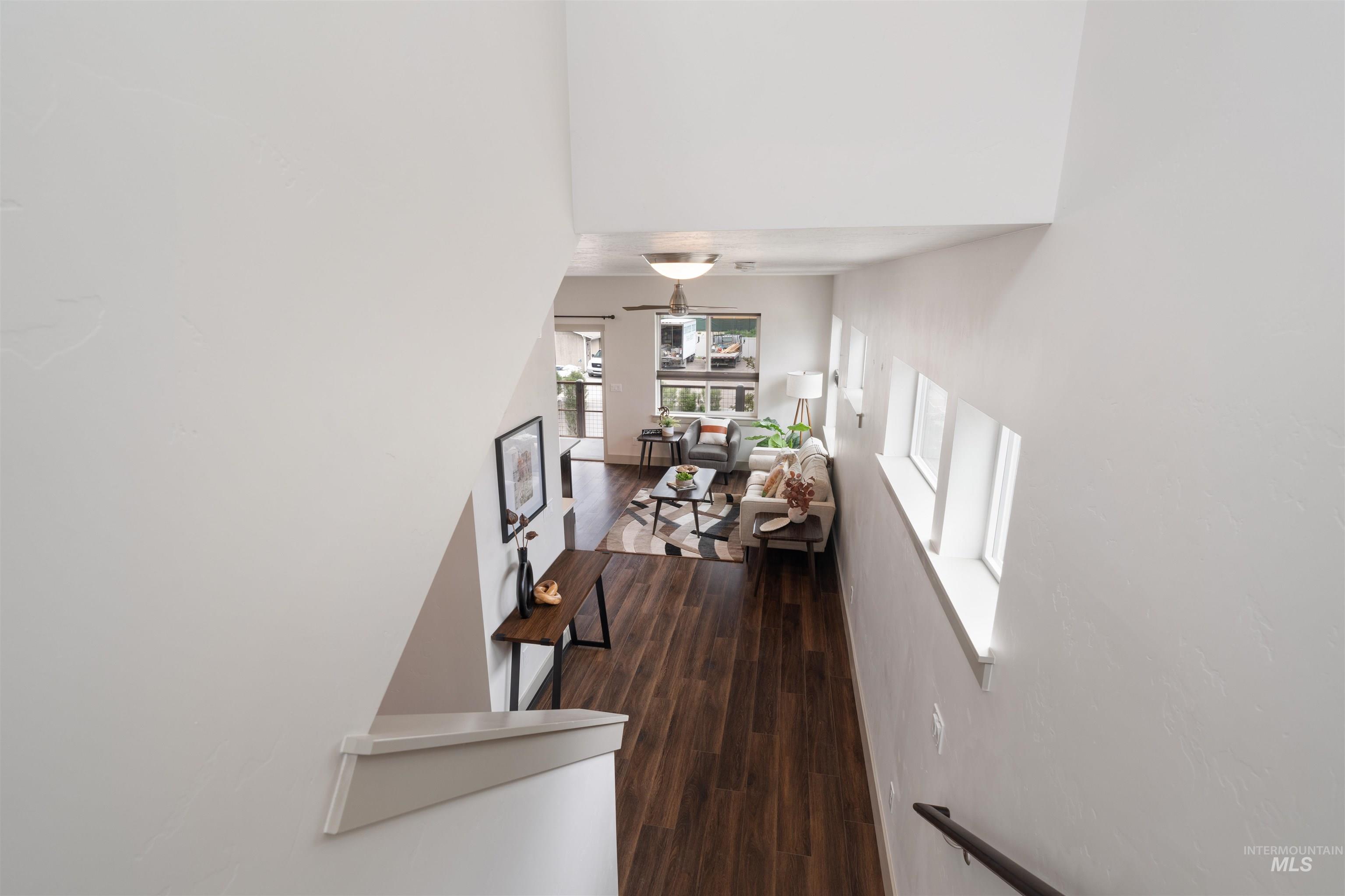 Open-concept living area with wood-finish flooring, a contemporary ceiling fan, and multiple windows providing natural illumination