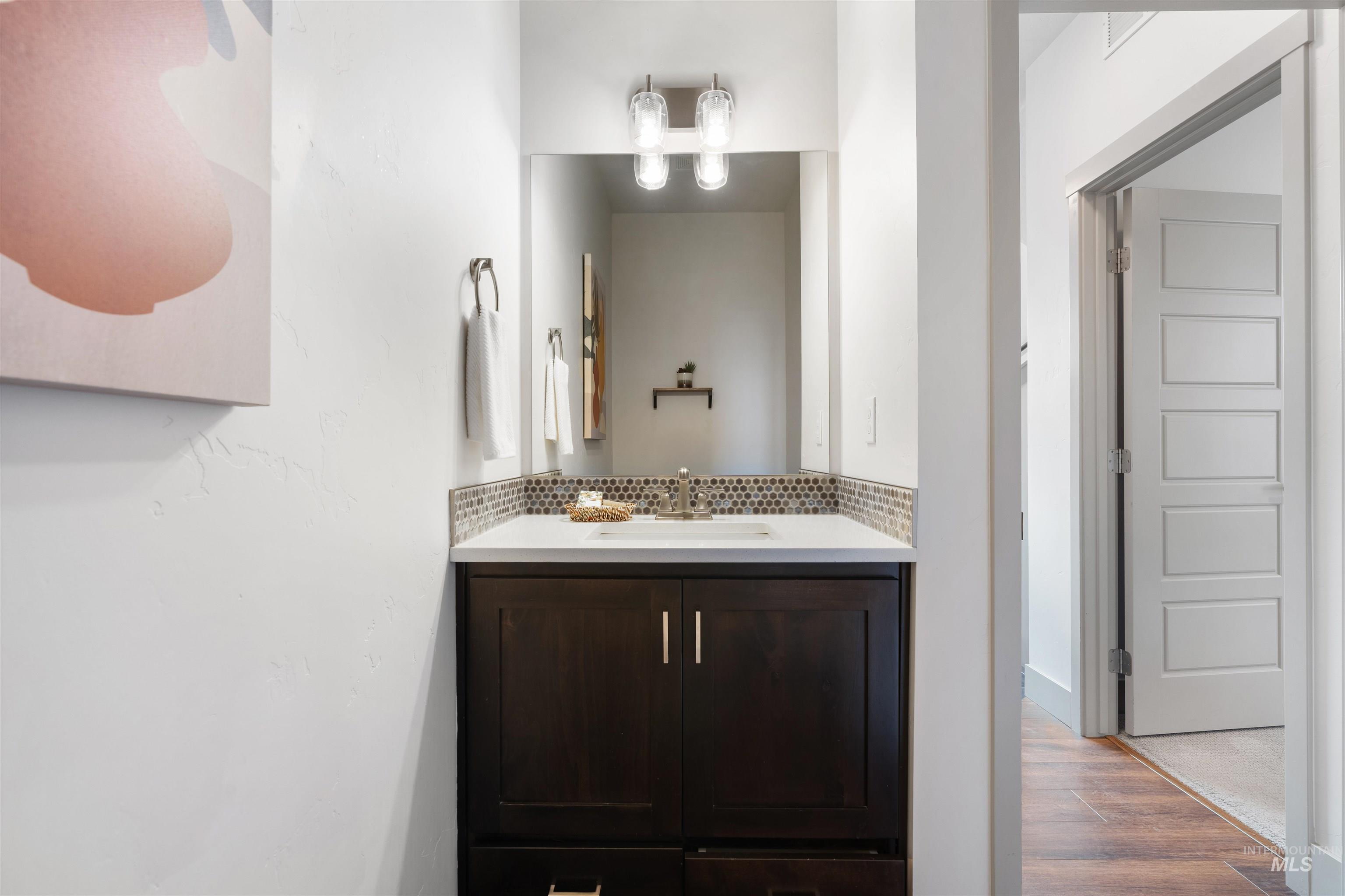 Dark wood-finish vanity with a white countertop, hexagon mosaic tile backsplash, and a polished chrome faucet