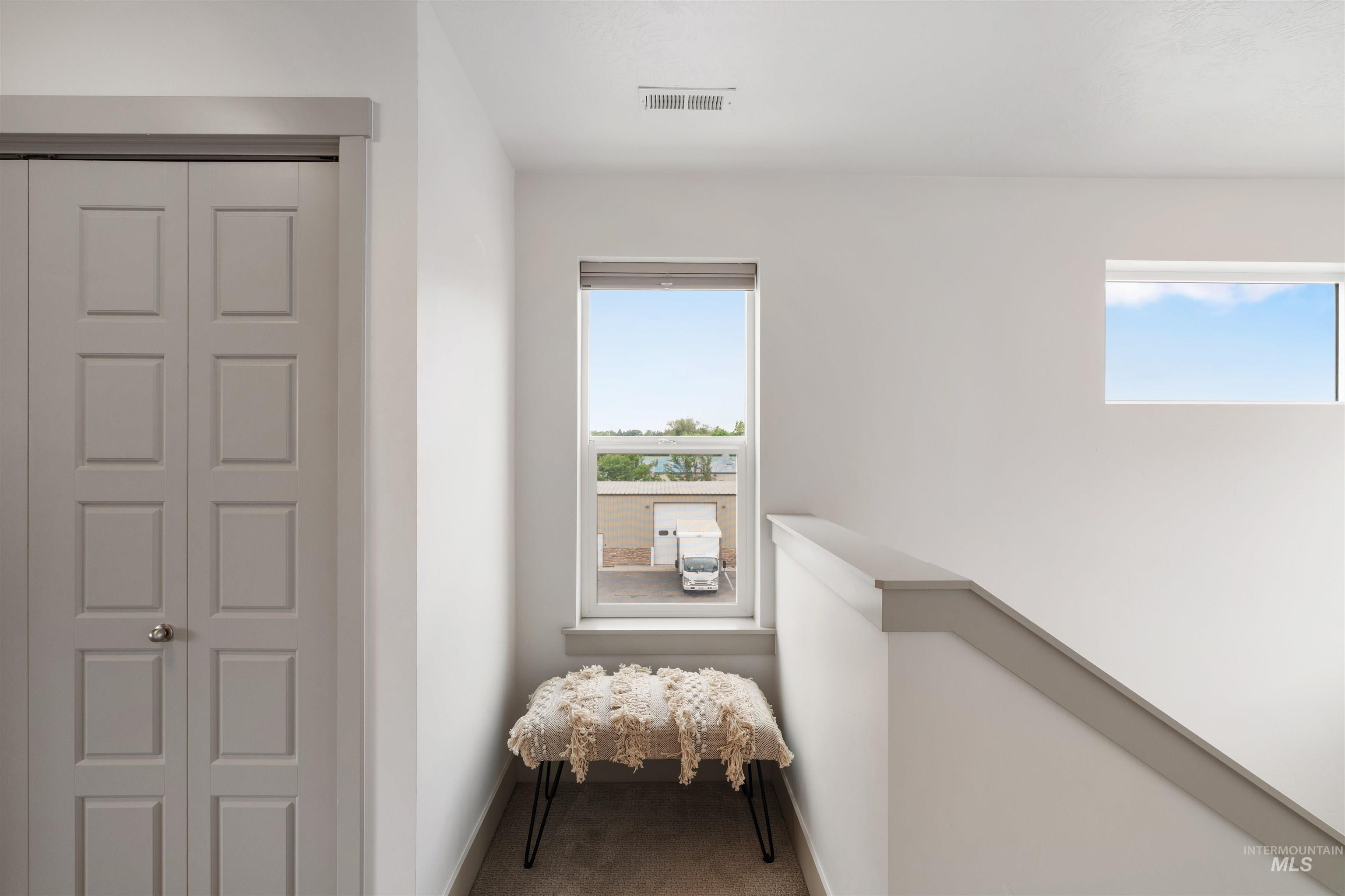 Upper-level hallway featuring a bi-fold door with multiple recessed panels, two distinct windows, and a staircase with a cap railing