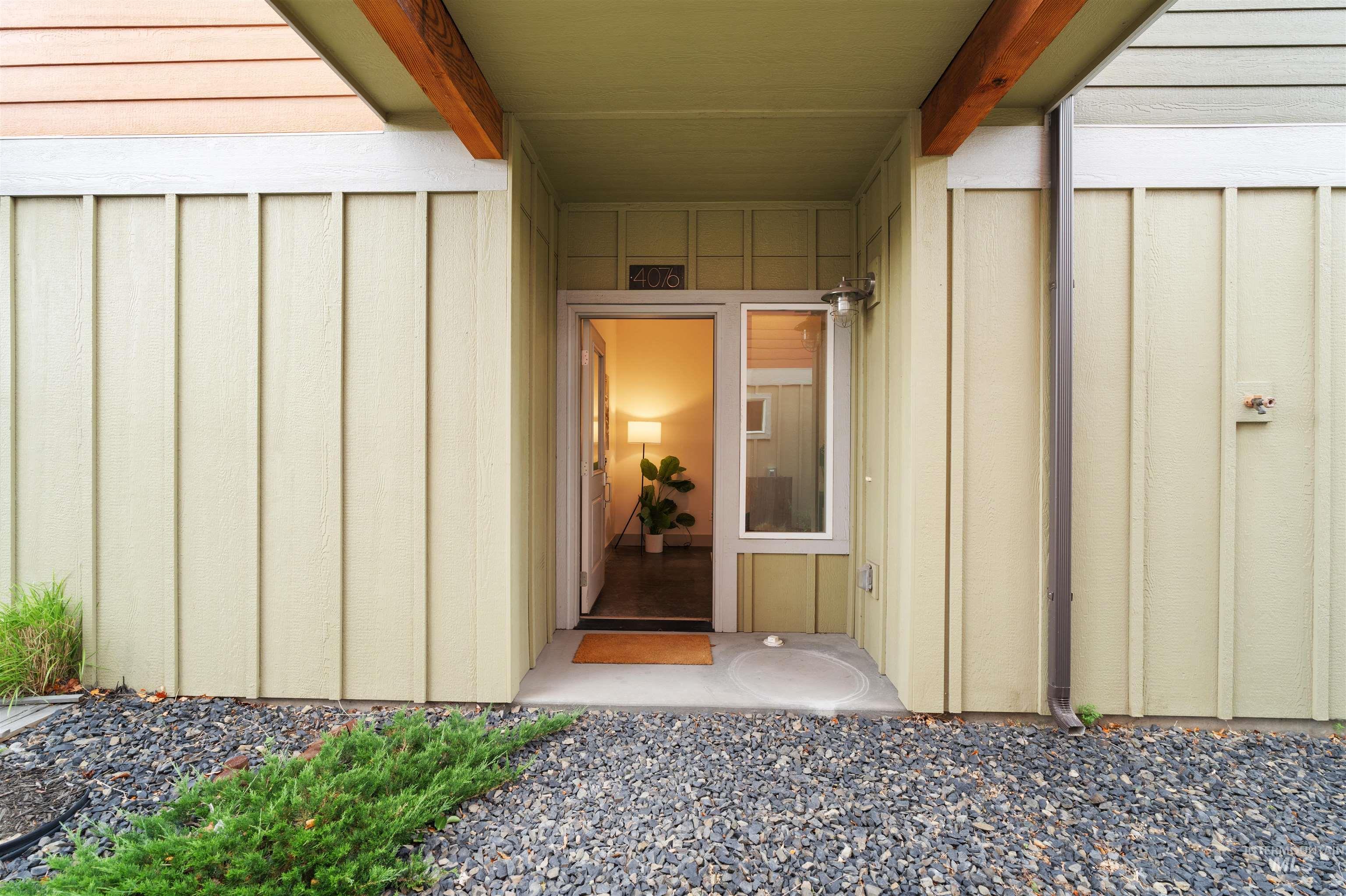 Inviting entryway featuring board and batten siding, exposed wood beams, and a concrete pathway