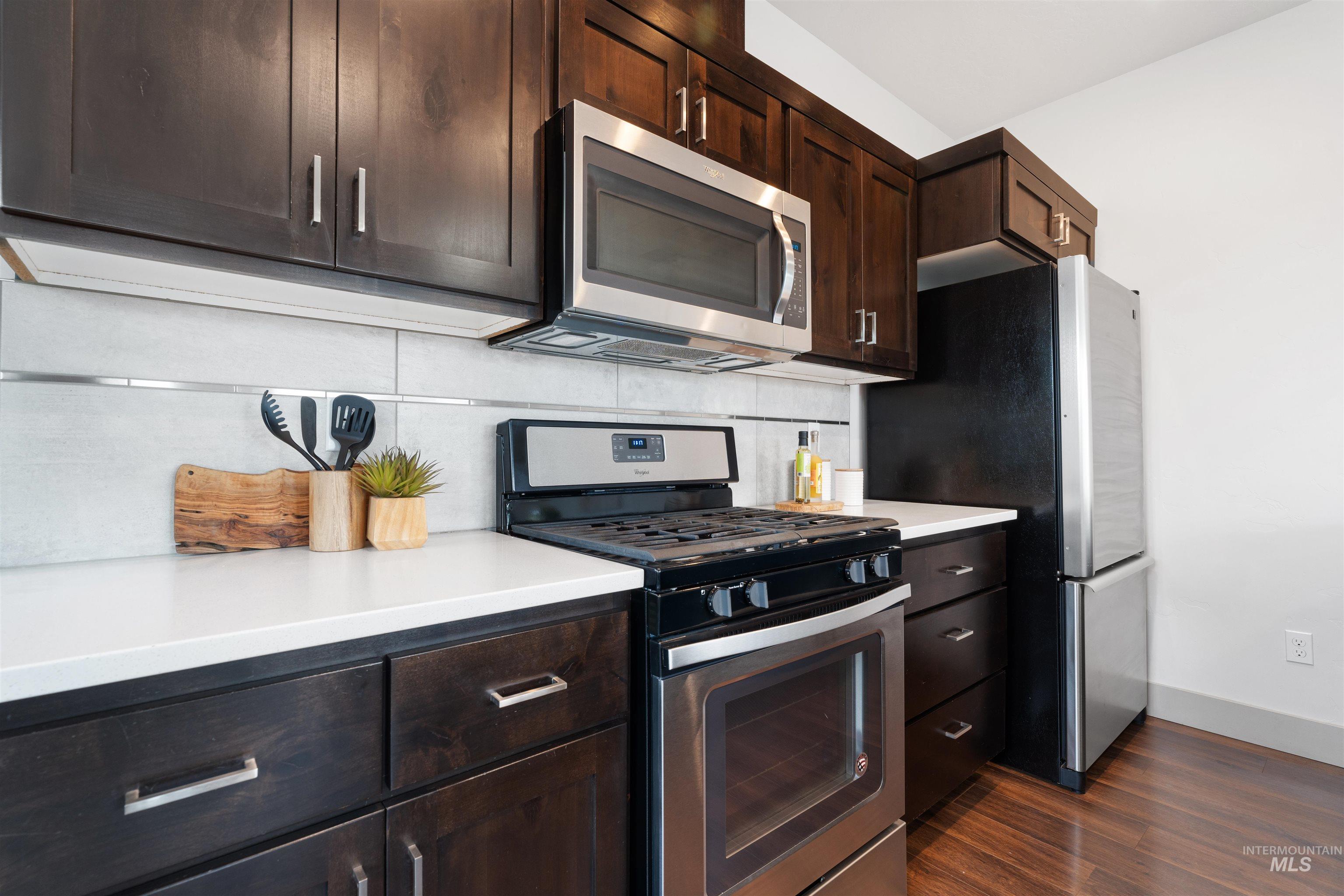 Kitchen featuring dark wood cabinetry, stainless steel appliances, light countertops, and a subway tile backsplash with horizontal accent strips