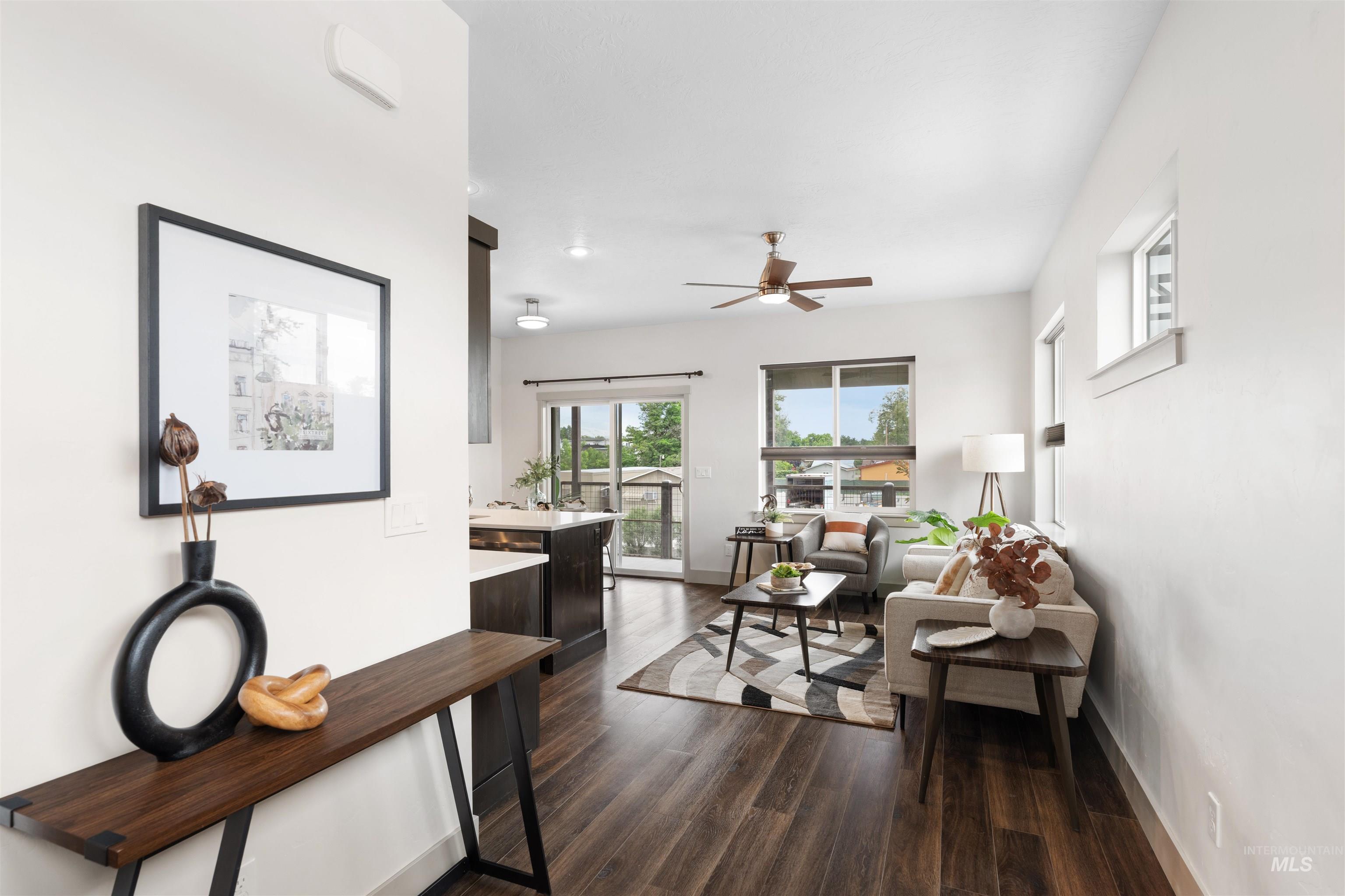 Open-concept living area featuring wood-finish flooring, a ceiling fan, and abundant natural light from multiple windows