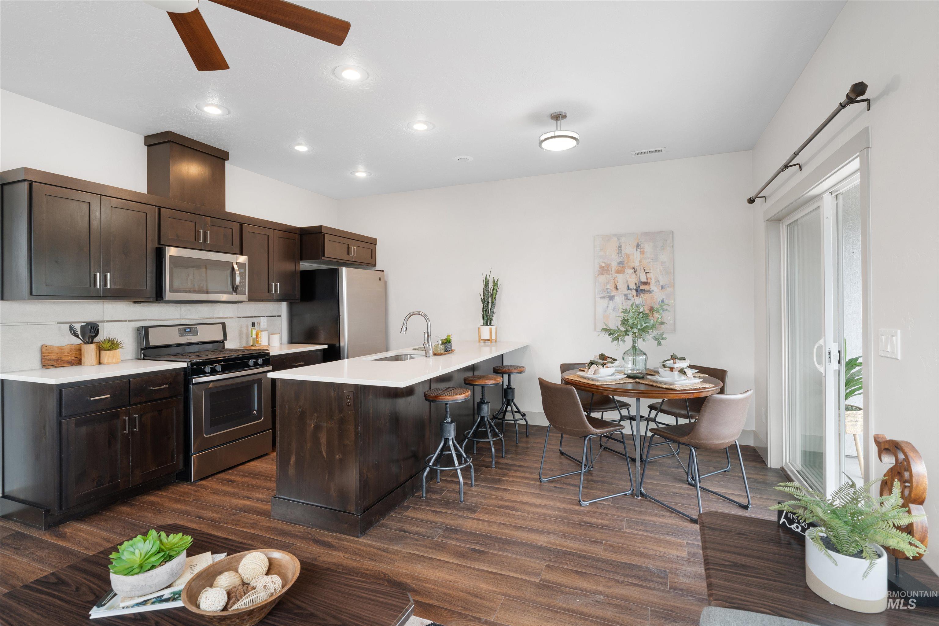 Open-concept kitchen and dining area featuring dark wood-finish cabinetry, stainless steel appliances, a center island with countertop seating, and wood-finish flooring throughout