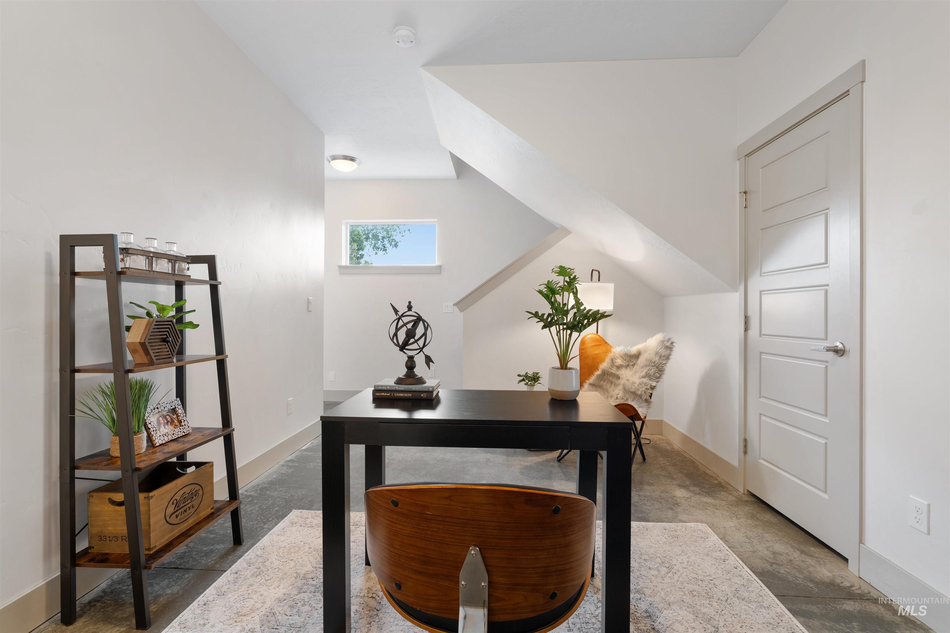 Versatile room featuring polished concrete flooring, white walls, a contemporary four-panel interior door, a transom window, and an overhead light fixture