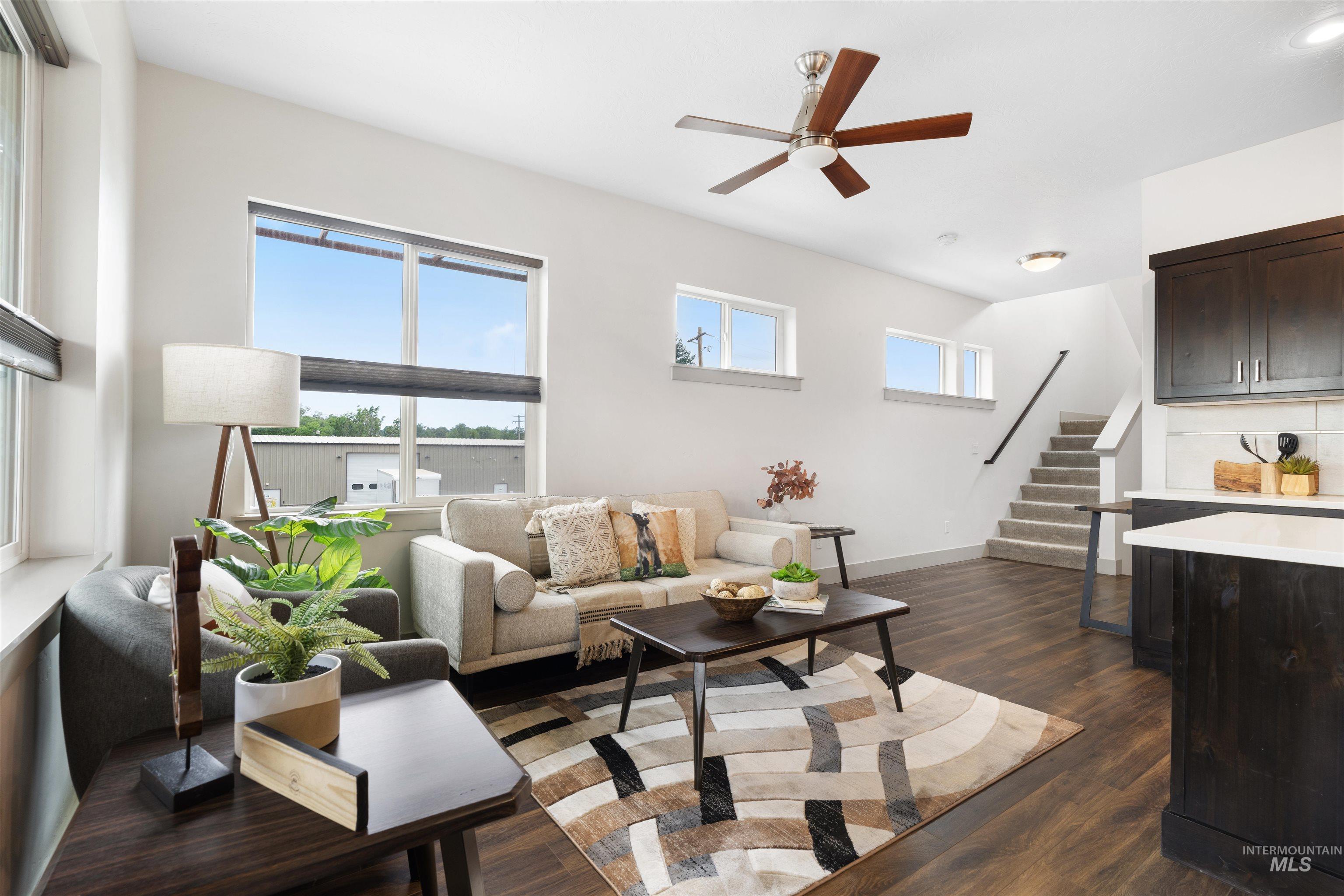 Open-concept living area featuring wood-finish flooring, a contemporary ceiling fan, and multiple windows providing ample natural light
