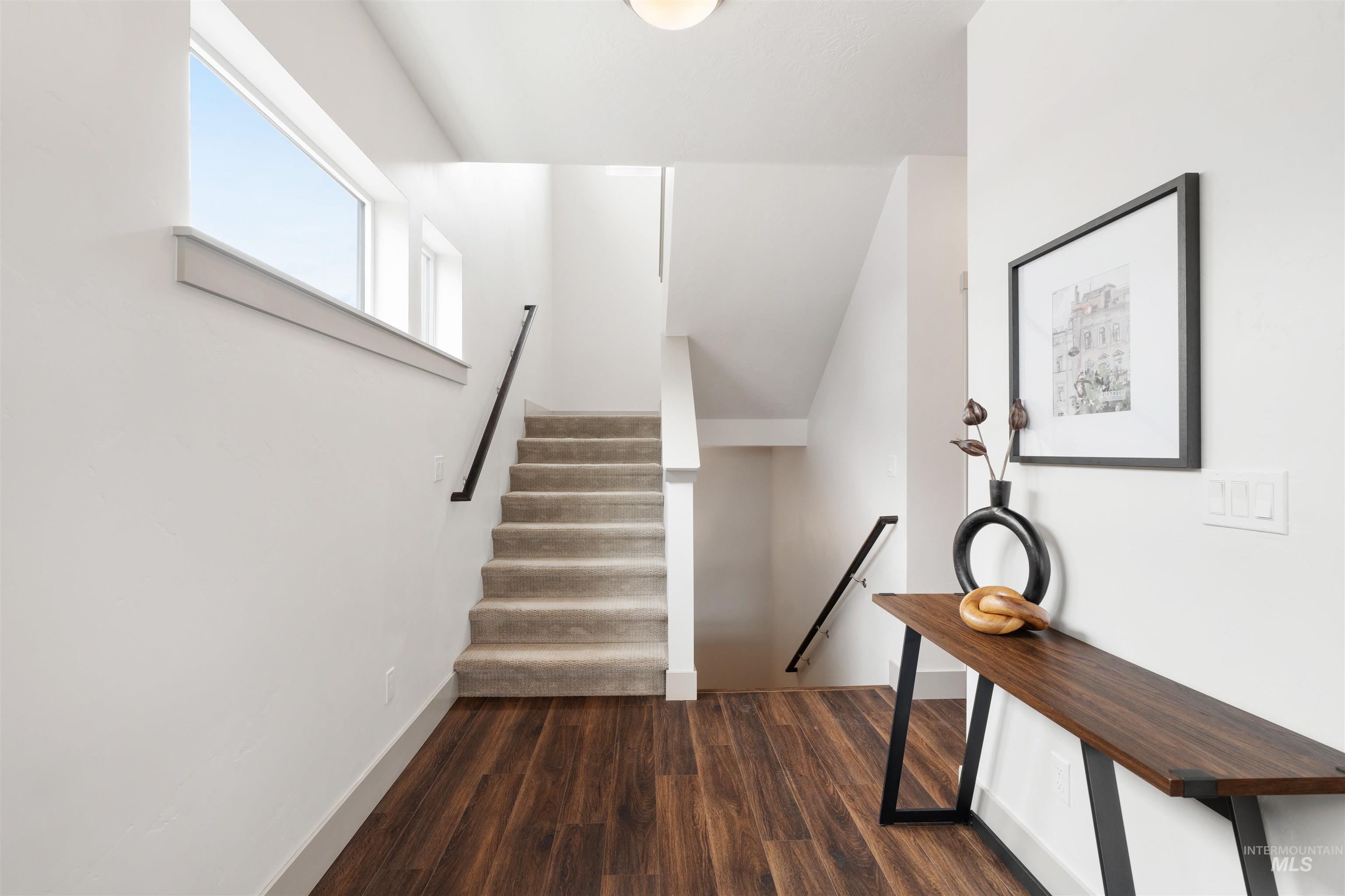Multilevel interior featuring wood-finish flooring, a carpeted staircase with dark handrails, and a large horizontal window providing natural light