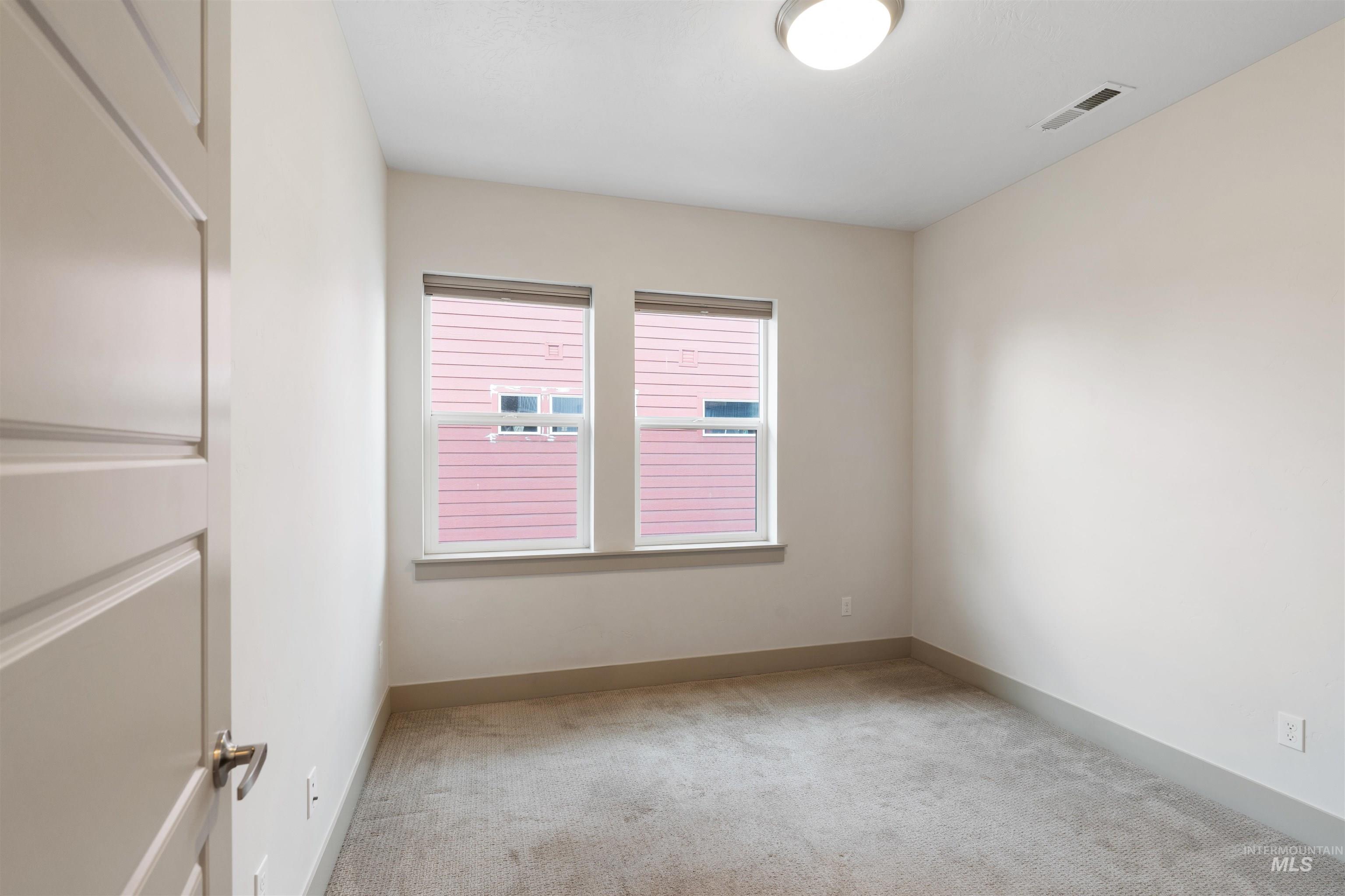 Neutral-toned room featuring a light carpeted floor and two windows with blinds