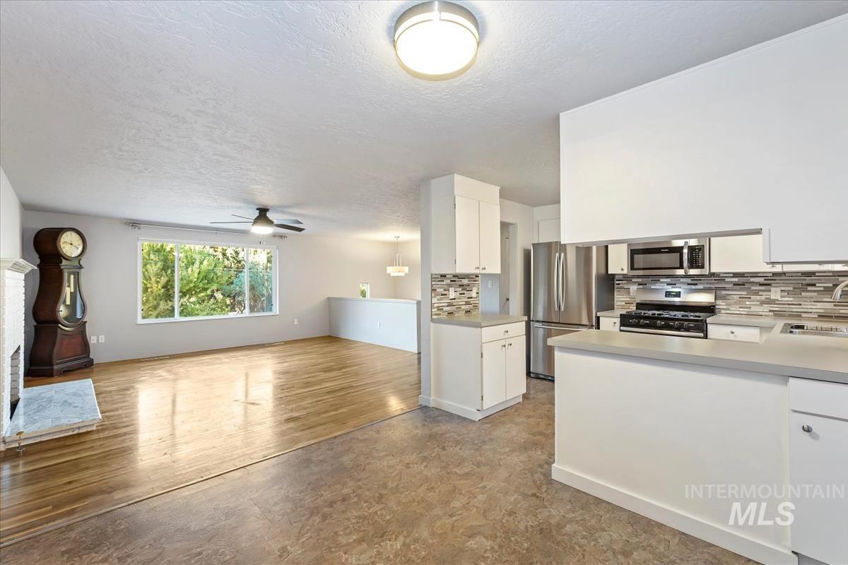 Kitchen featuring open floor plan, a textured ceiling, light countertops, stainless steel appliances, and decorative backsplash