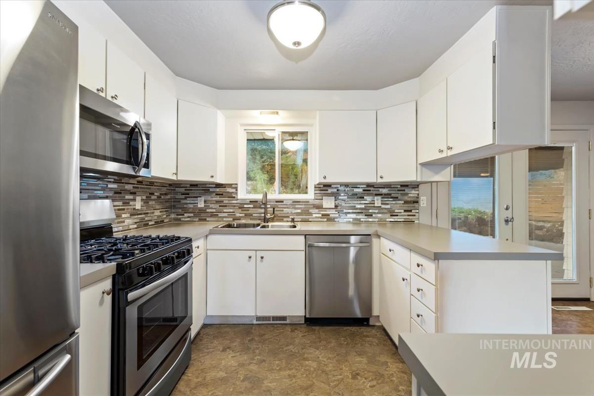 Kitchen with appliances with stainless steel finishes, light countertops, a peninsula, and white cabinetry