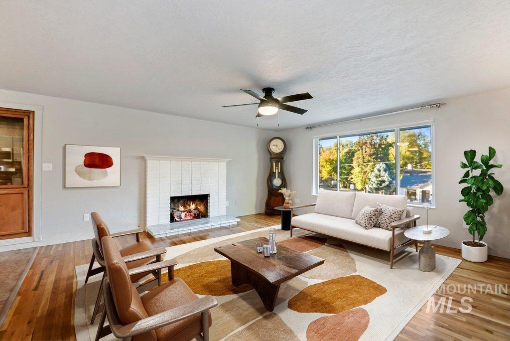 Living area with light wood finished floors, a fireplace, a textured ceiling, and a ceiling fan