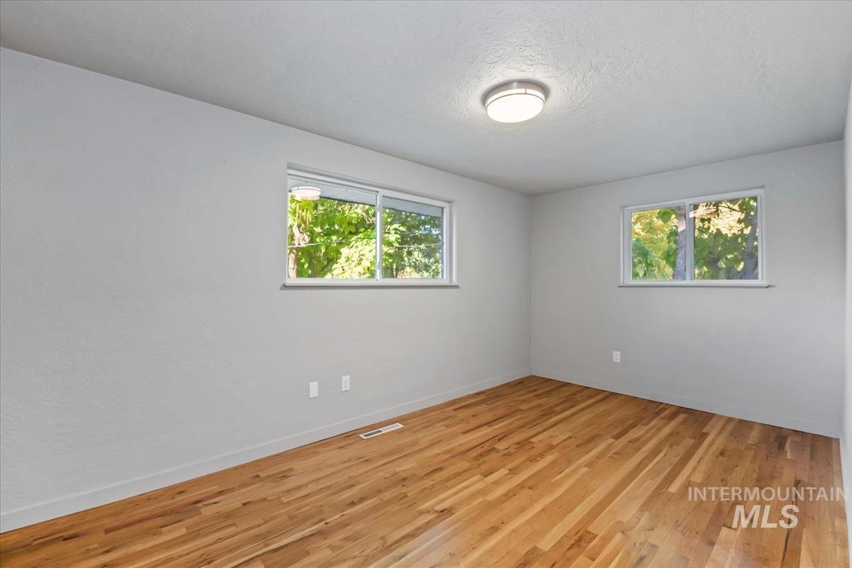 Unfurnished room with healthy amount of natural light, light wood finished floors, and a textured ceiling