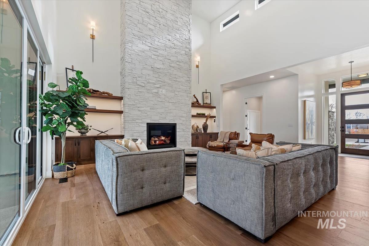 Living room featuring a towering ceiling, light wood-type flooring, and a stone fireplace