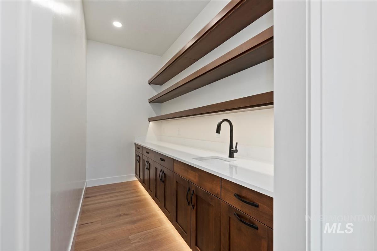 Bar area with open shelves, dark brown cabinets, light wood-type flooring, light stone countertops, and recessed lighting