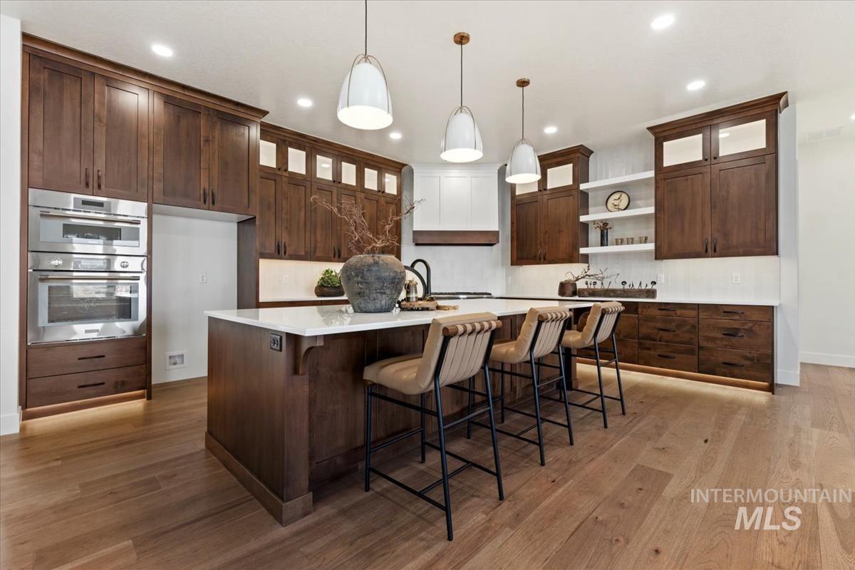 Kitchen featuring glass insert cabinets, a breakfast bar, dark brown cabinetry, open shelves, and double oven