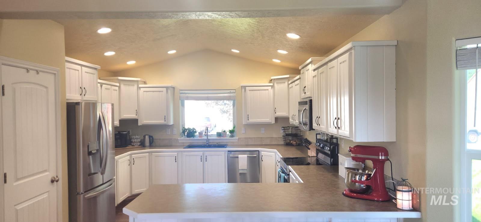 Kitchen featuring stainless steel appliances, vaulted ceiling, a peninsula, recessed lighting, and white cabinetry