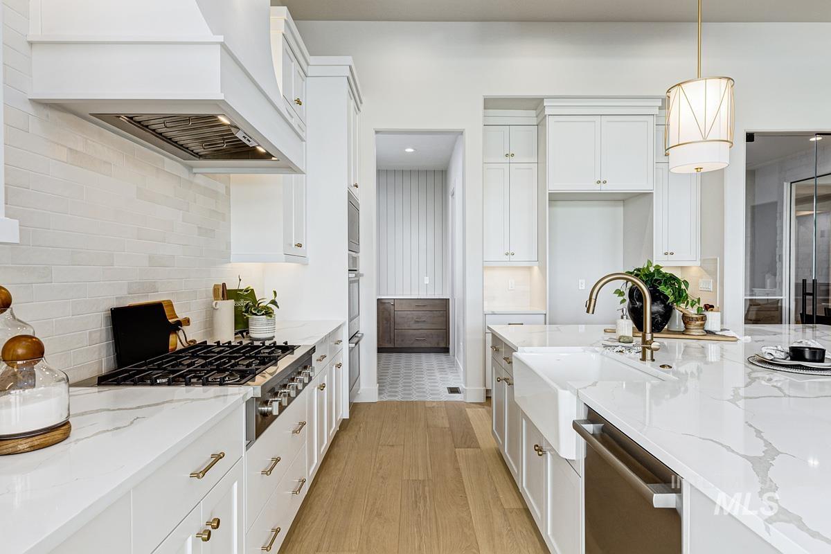 Kitchen with light stone countertops, stainless steel appliances, light wood finished floors, and hanging light fixtures