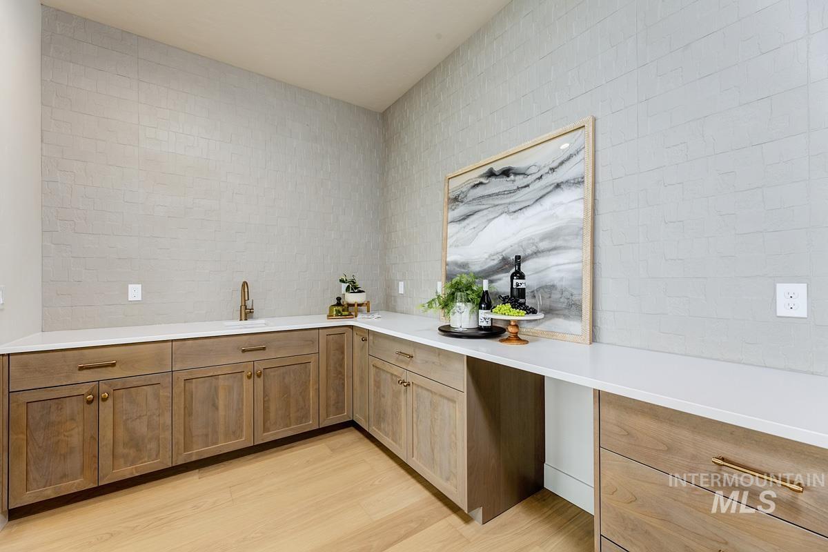 Bar featuring light wood-style flooring, light stone countertops, and wood finish cabinets