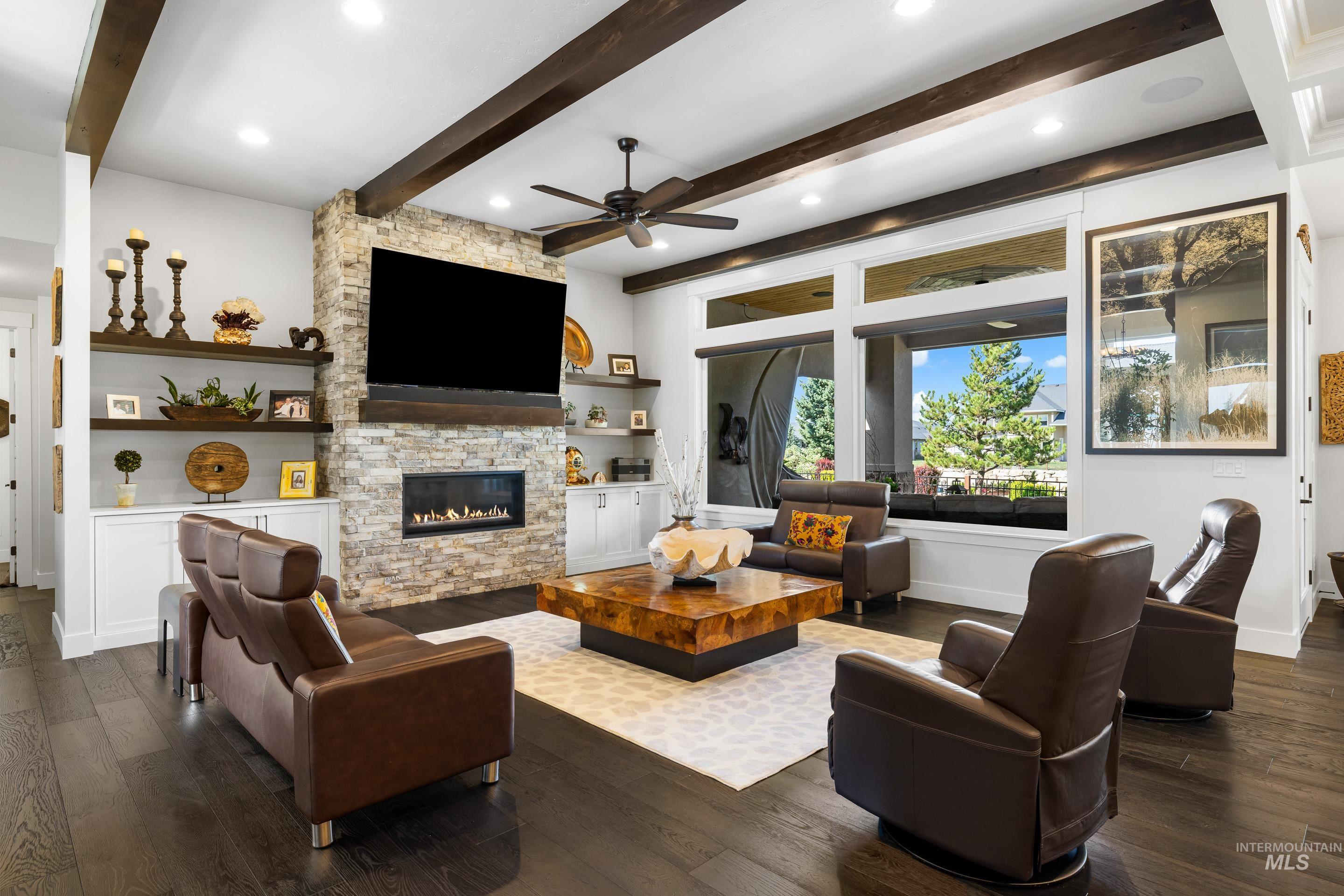 Living area featuring dark wood-type flooring, a ceiling fan, a stone fireplace, beamed ceiling, and recessed lighting