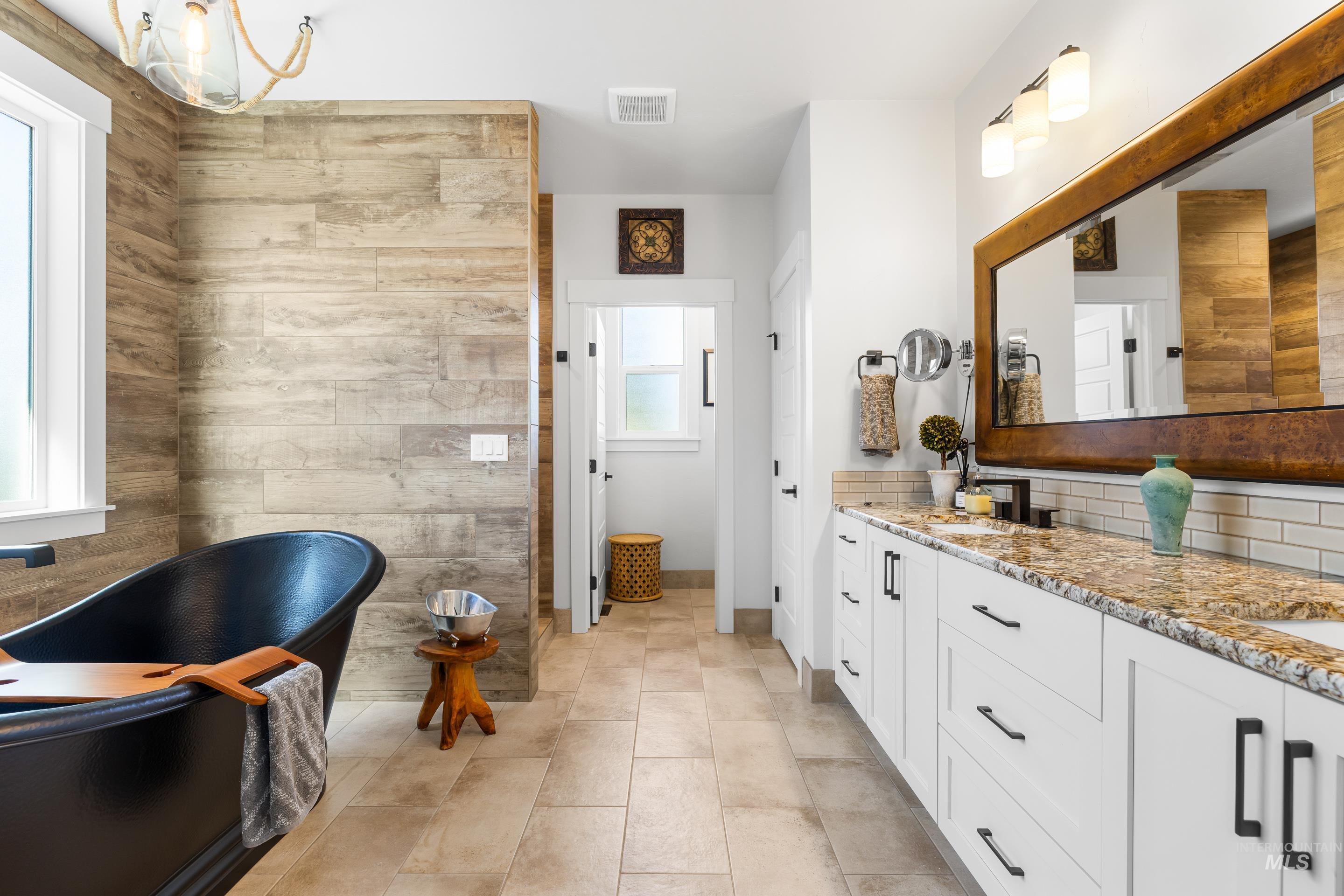 Bathroom with a soaking tub, double vanity, light tile patterned floors, and backsplash