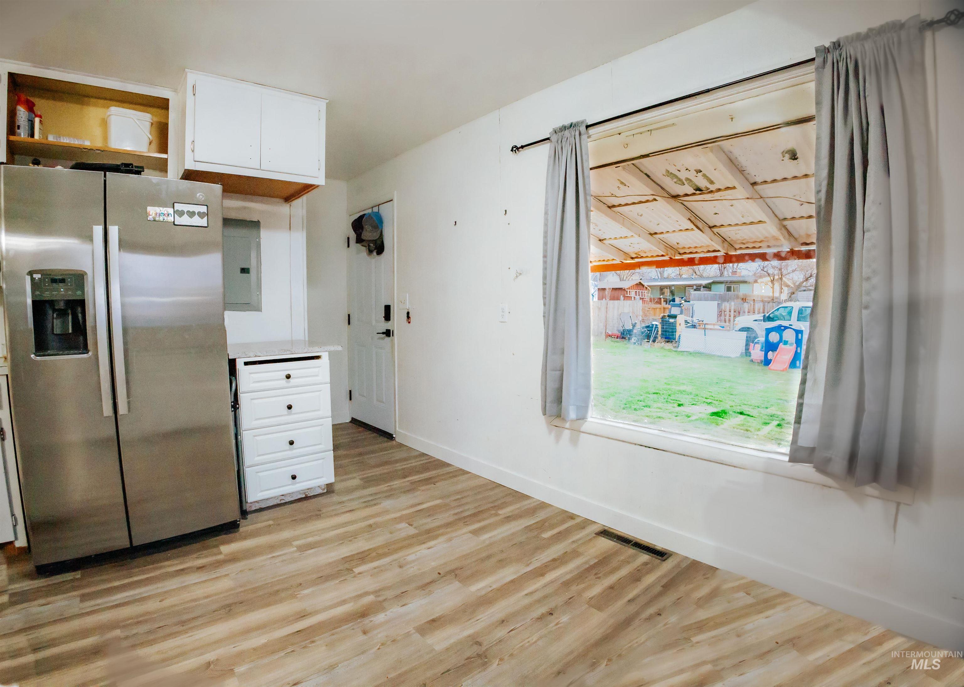 Kitchen with stainless steel fridge with ice dispenser, white cabinetry, light wood finished floors, electric panel, and open shelves