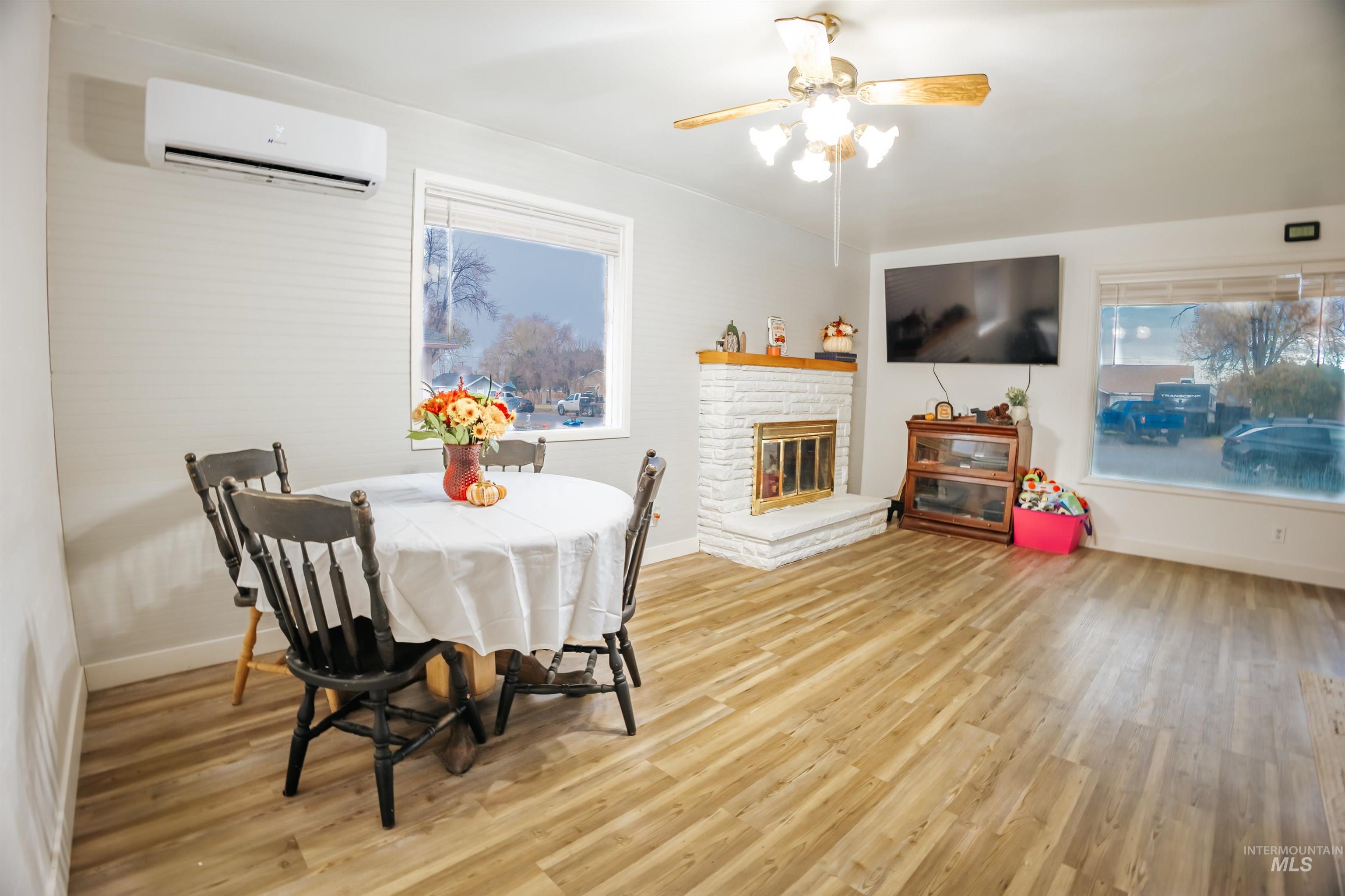 Dining room with a brick fireplace, light wood-type flooring, a wall mounted air conditioner, and healthy amount of natural light