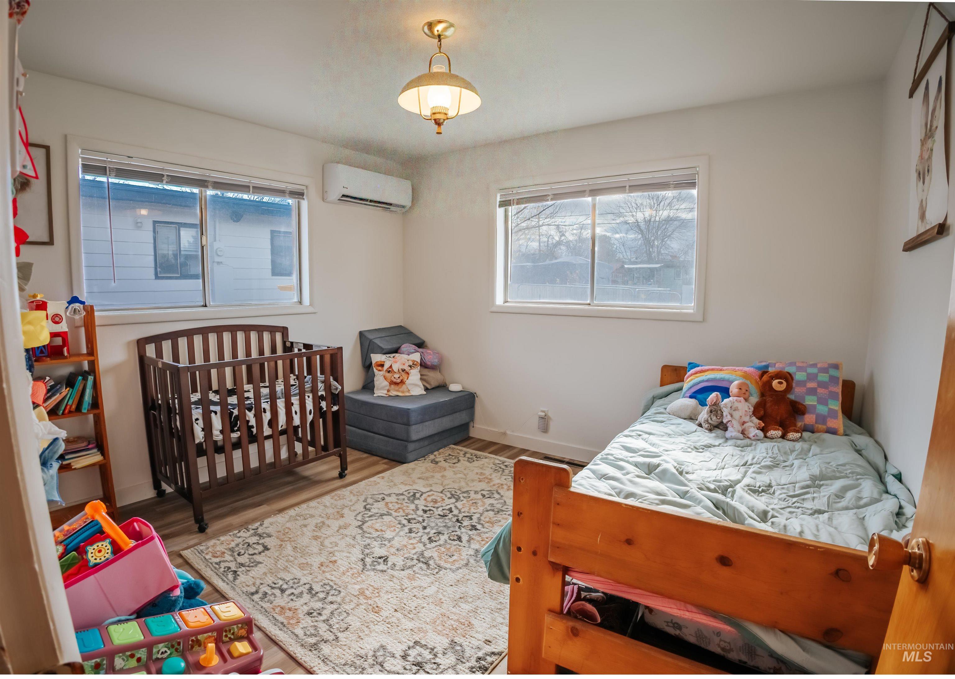 Bedroom with wood finished floors, multiple windows, a wall mounted AC, and a crib