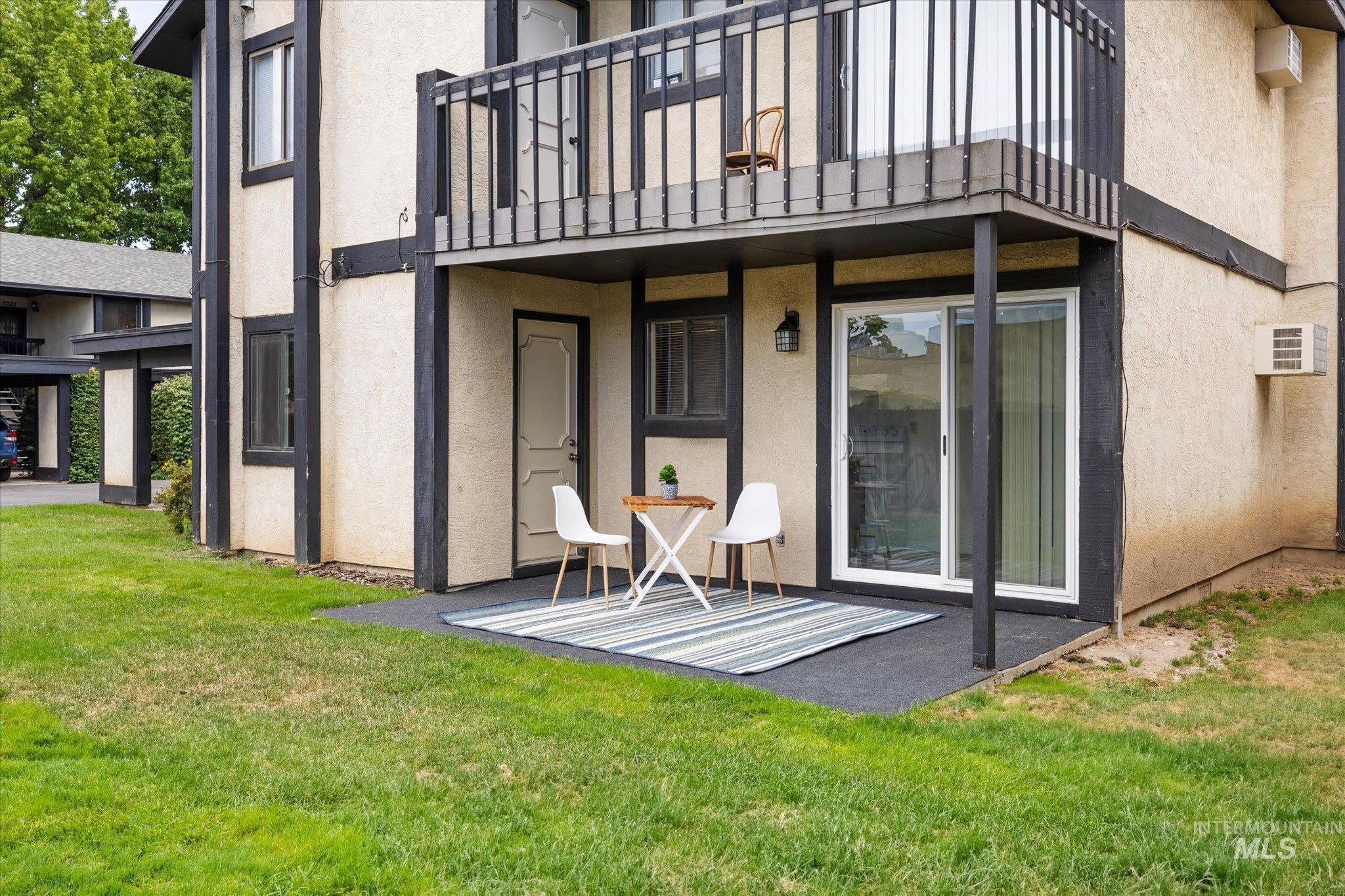 Back of house featuring a balcony, stucco siding, a yard, and a patio