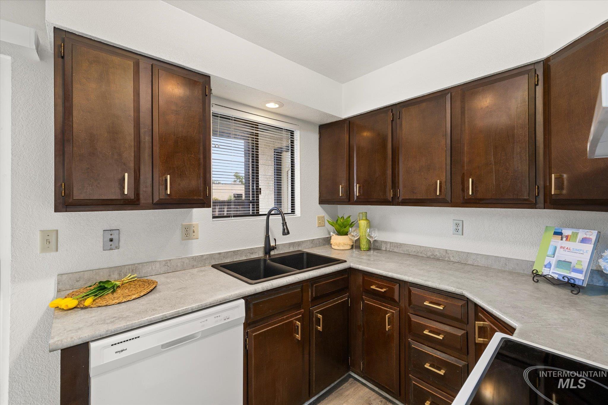 Kitchen with white dishwasher, dark brown cabinetry, light countertops, black electric stovetop, and a textured wall