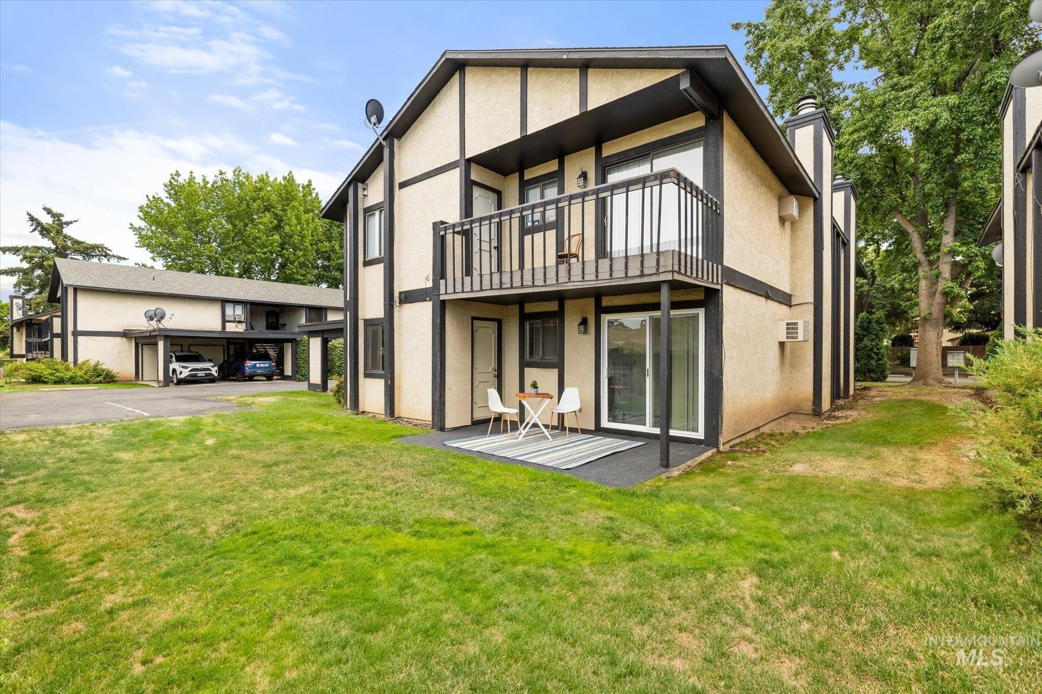 Rear view of property featuring a balcony, stucco siding, a lawn, and covered and uncovered parking
