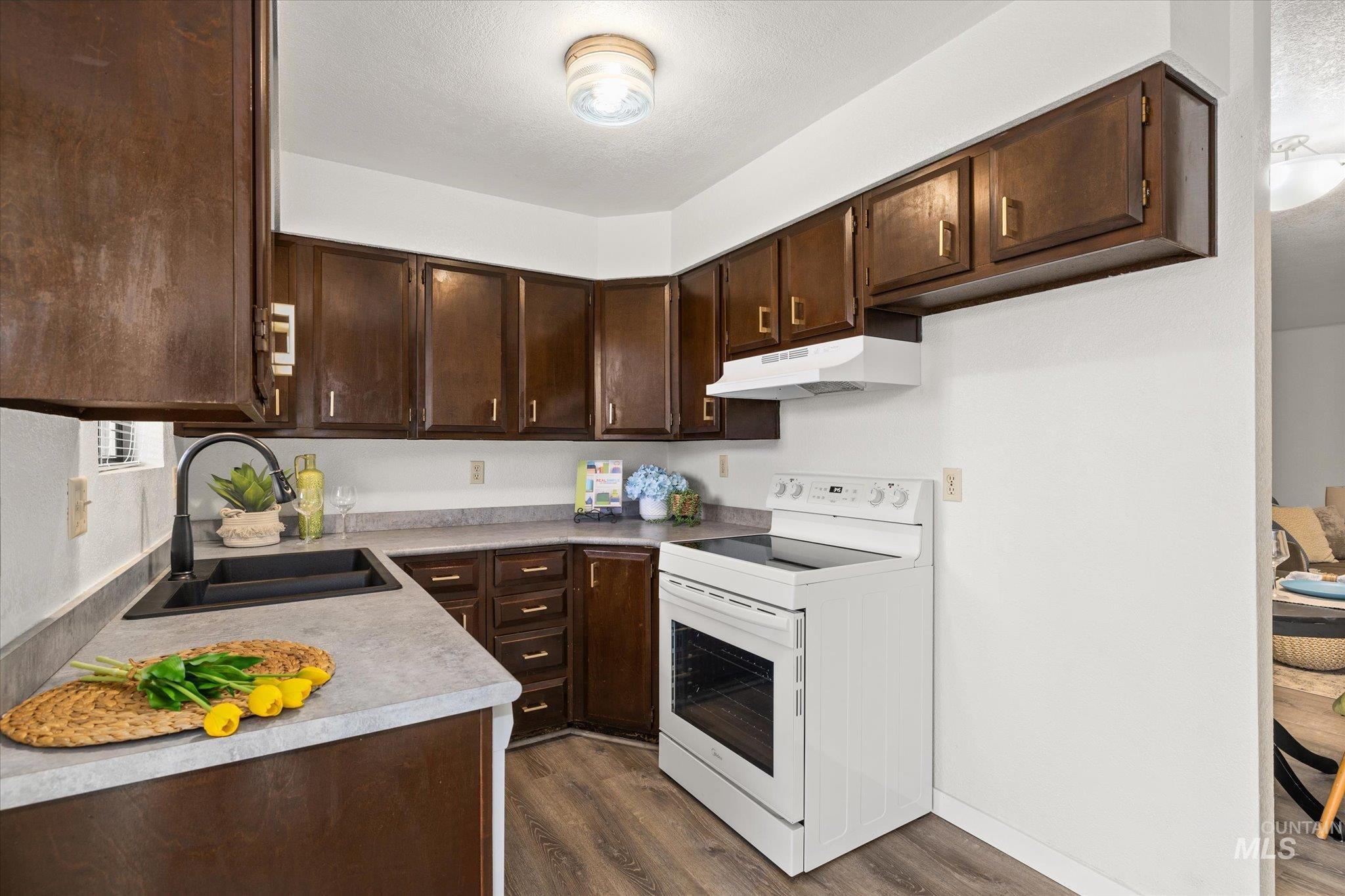 Kitchen with white range with electric cooktop, dark brown cabinetry, dark wood-style floors, and under cabinet range hood