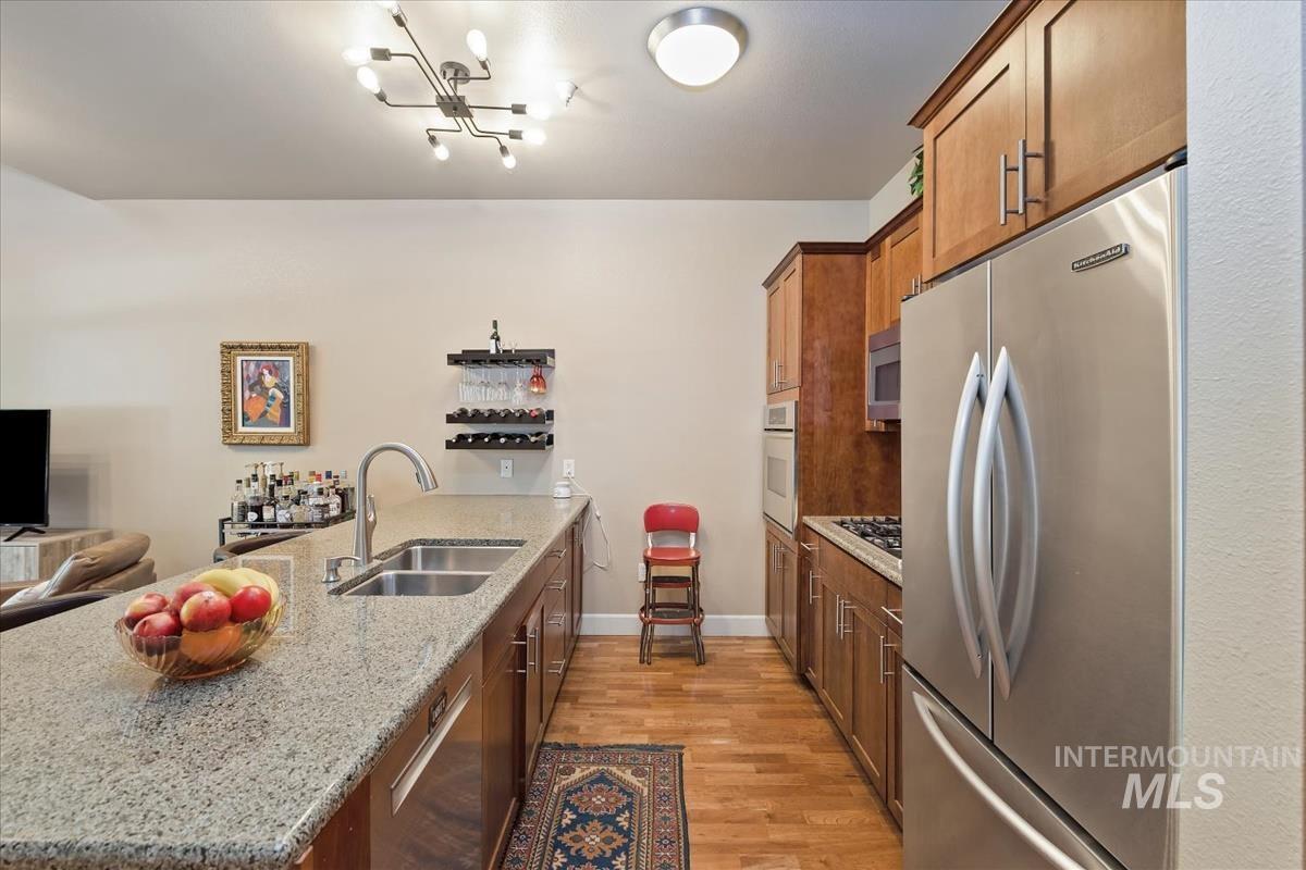Kitchen with brown cabinetry, a peninsula, stainless steel appliances, and light stone counters