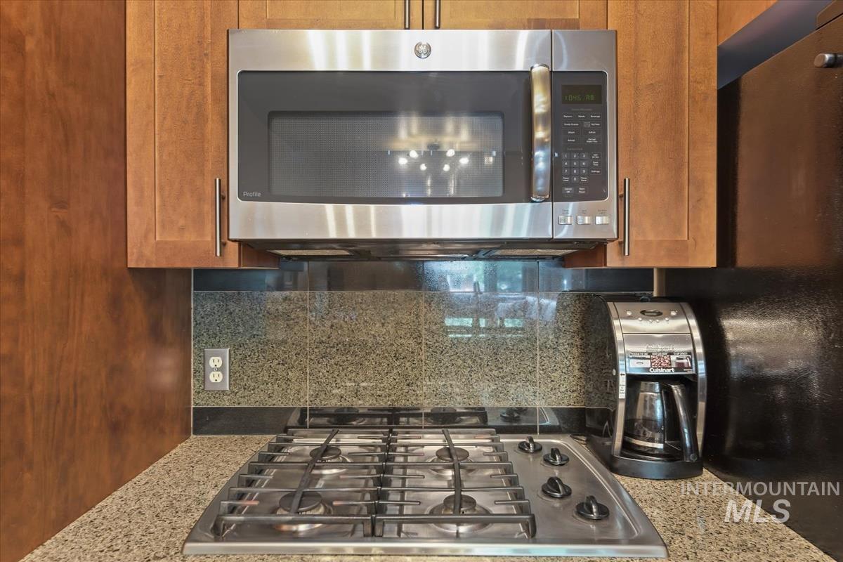 Kitchen featuring stainless steel appliances, decorative backsplash, light stone counters, and brown cabinetry