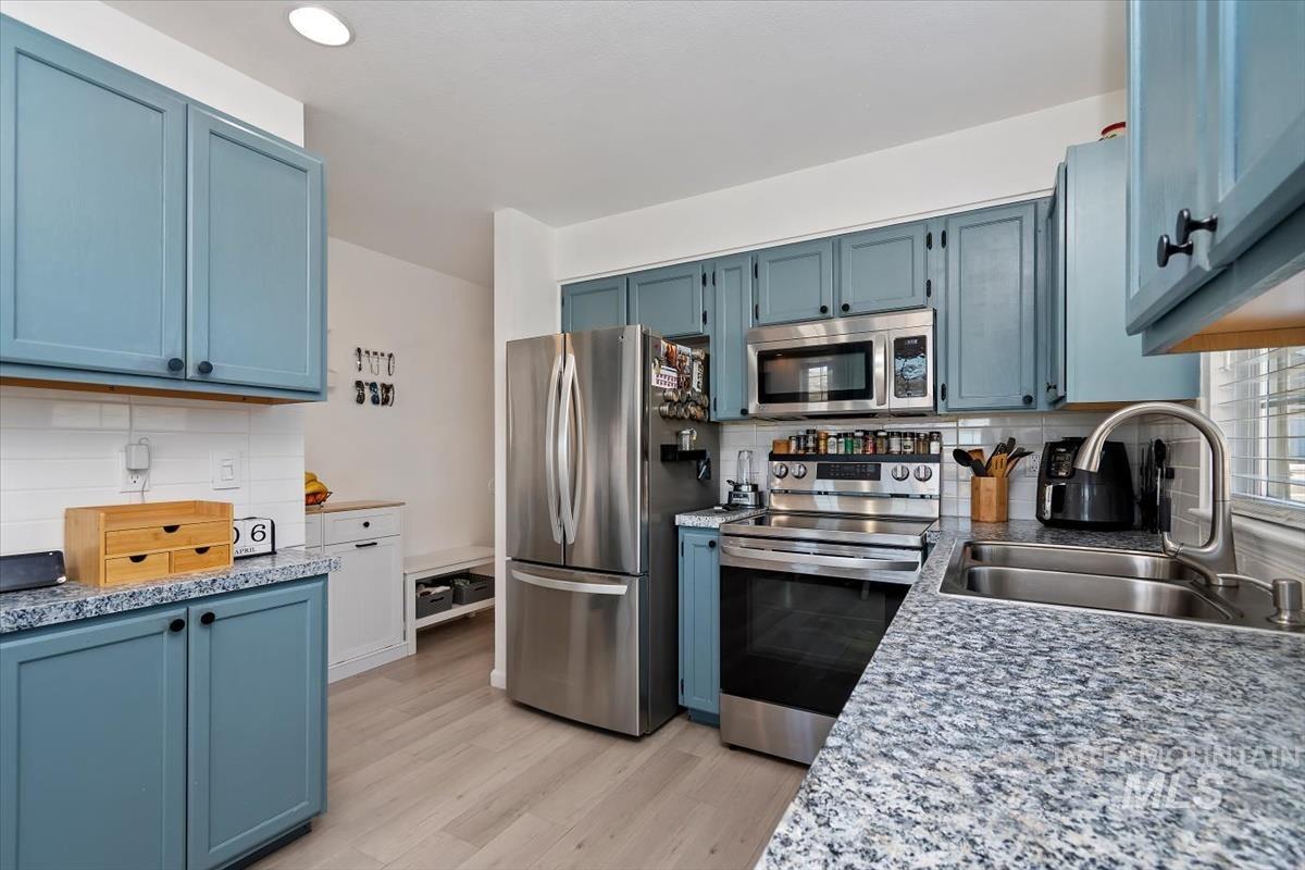 Kitchen with blue cabinets, stainless steel appliances, backsplash, and light wood-style flooring