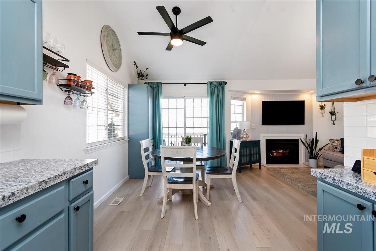 Dining area with a ceiling fan, light wood-type flooring, lofted ceiling, a warm lit fireplace, and healthy amount of natural light