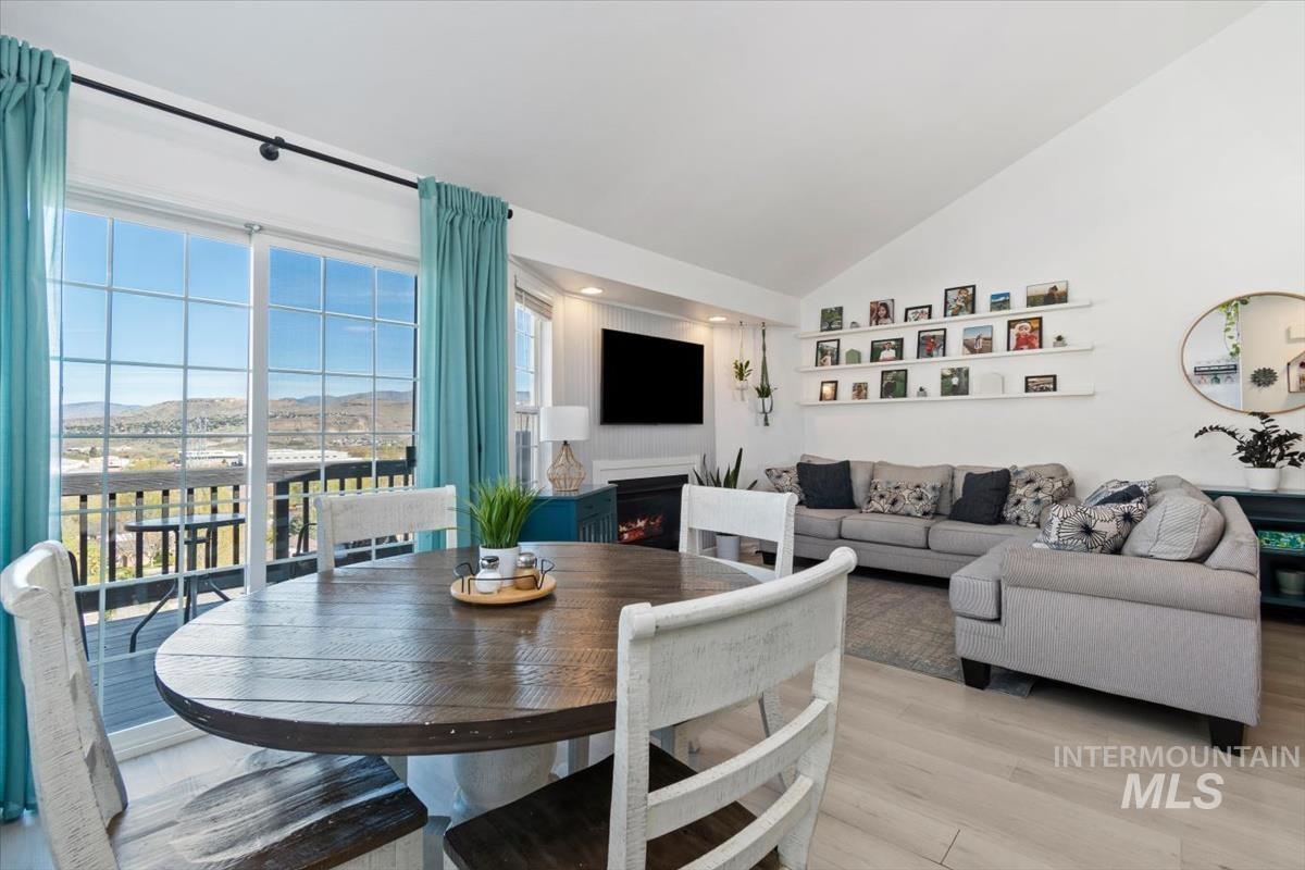 Dining room with a lit fireplace, light wood-style flooring, vaulted ceiling, and recessed lighting