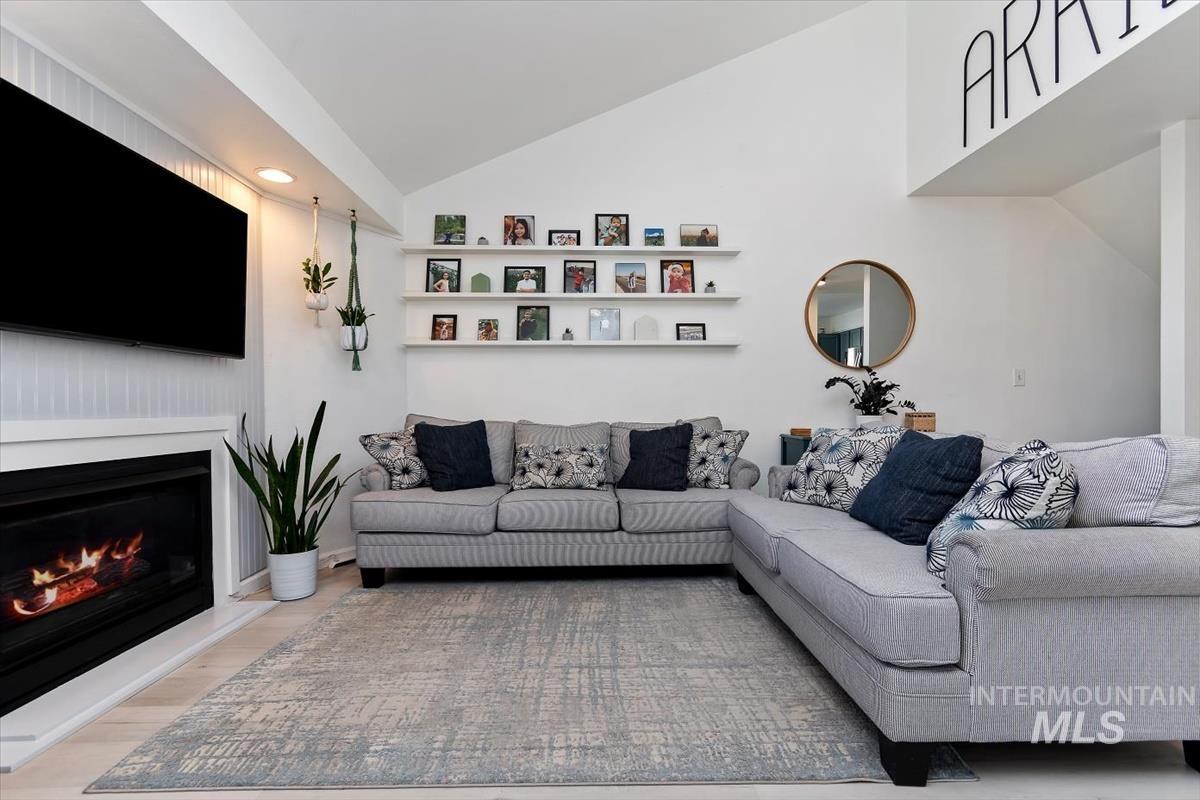 Living area with vaulted ceiling, light wood-type flooring, and a lit fireplace