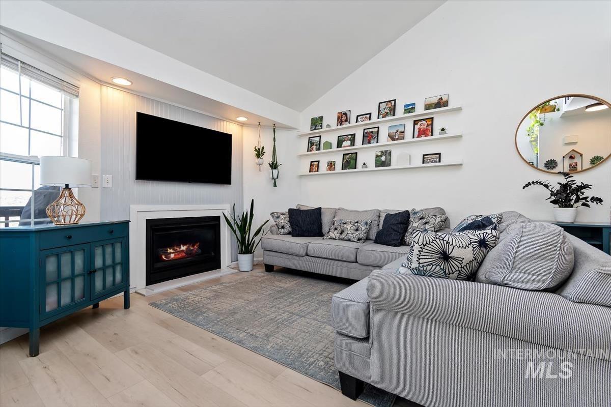Living room with light wood finished floors, vaulted ceiling, a warm lit fireplace, and recessed lighting