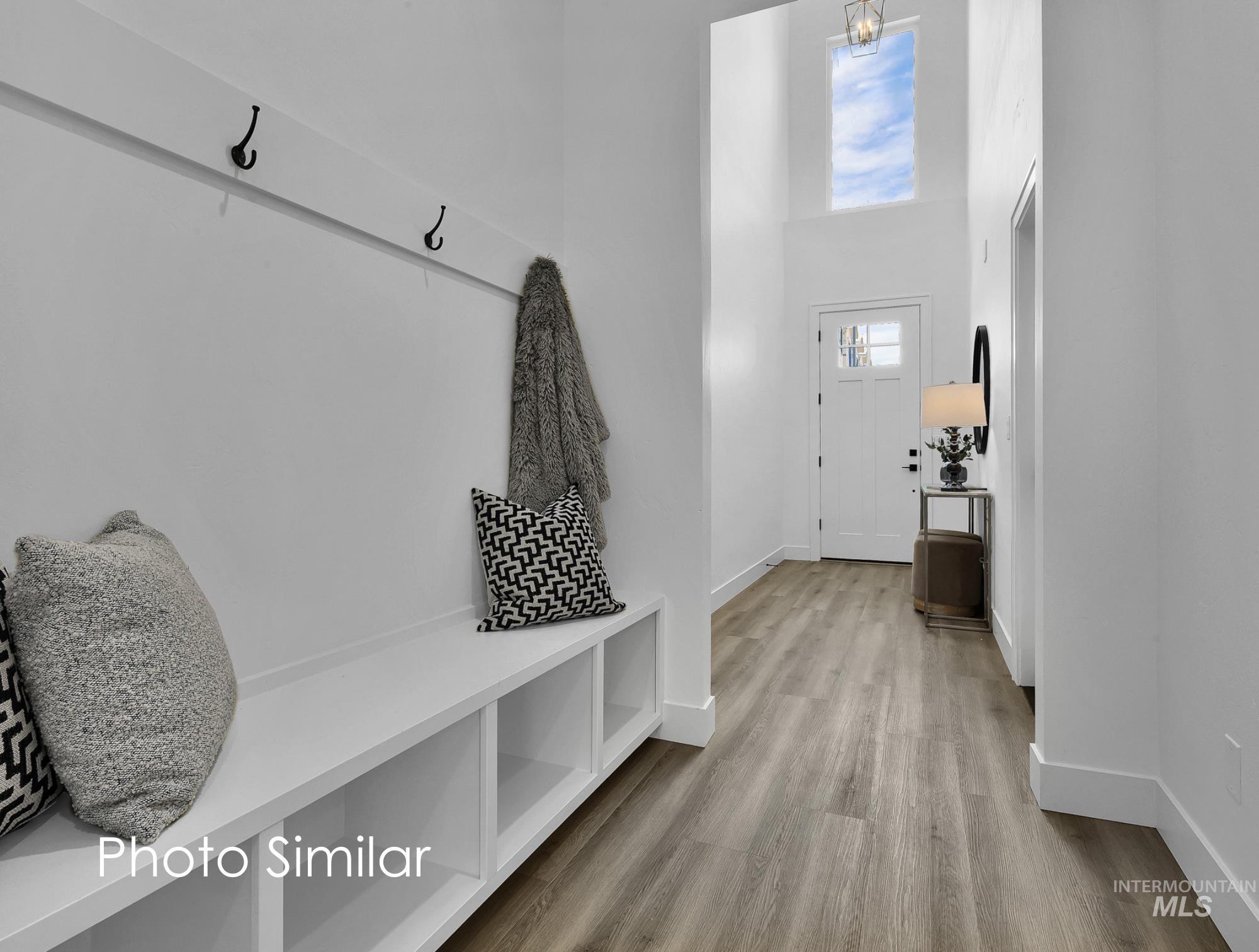 Entryway featuring high ceilings, a white paneled door with glass inserts, wood-finish flooring, and a built-in bench with storage cubbies and coat hooks