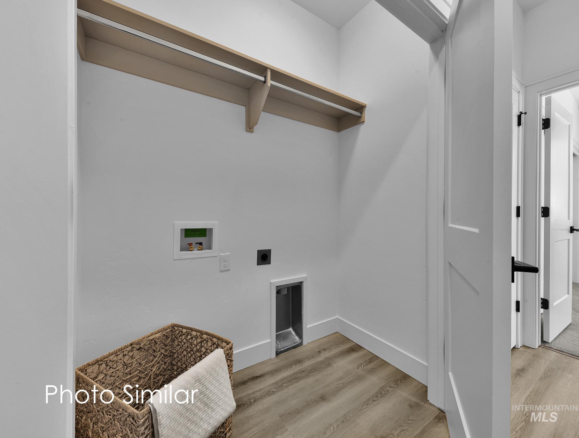 Dedicated laundry area featuring wood-finish flooring, a light wood shelf with hanging rod, and white baseboards