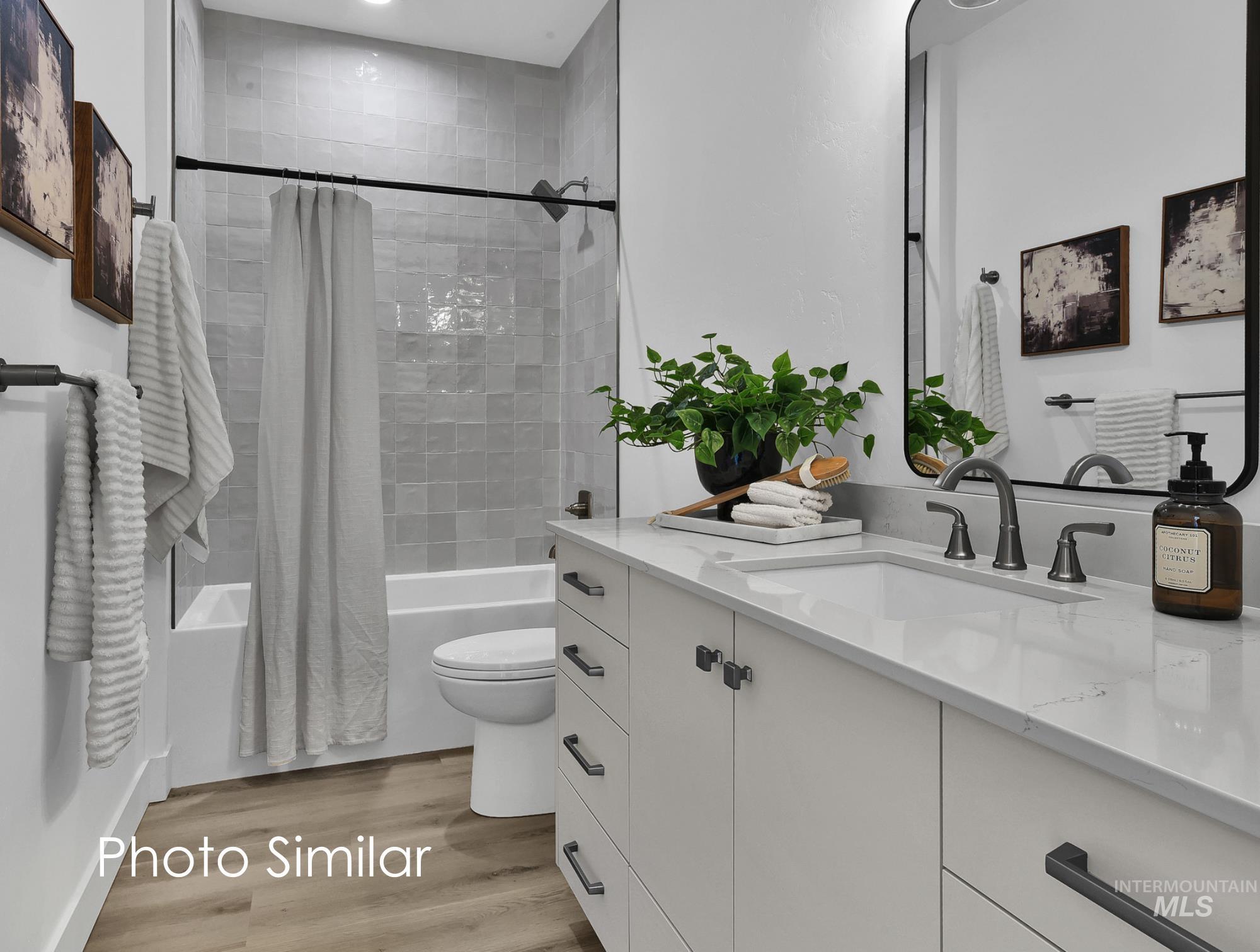Contemporary bathroom featuring a single vanity with a white countertop and undermount sink, dark-toned hardware, and wood-finish flooring