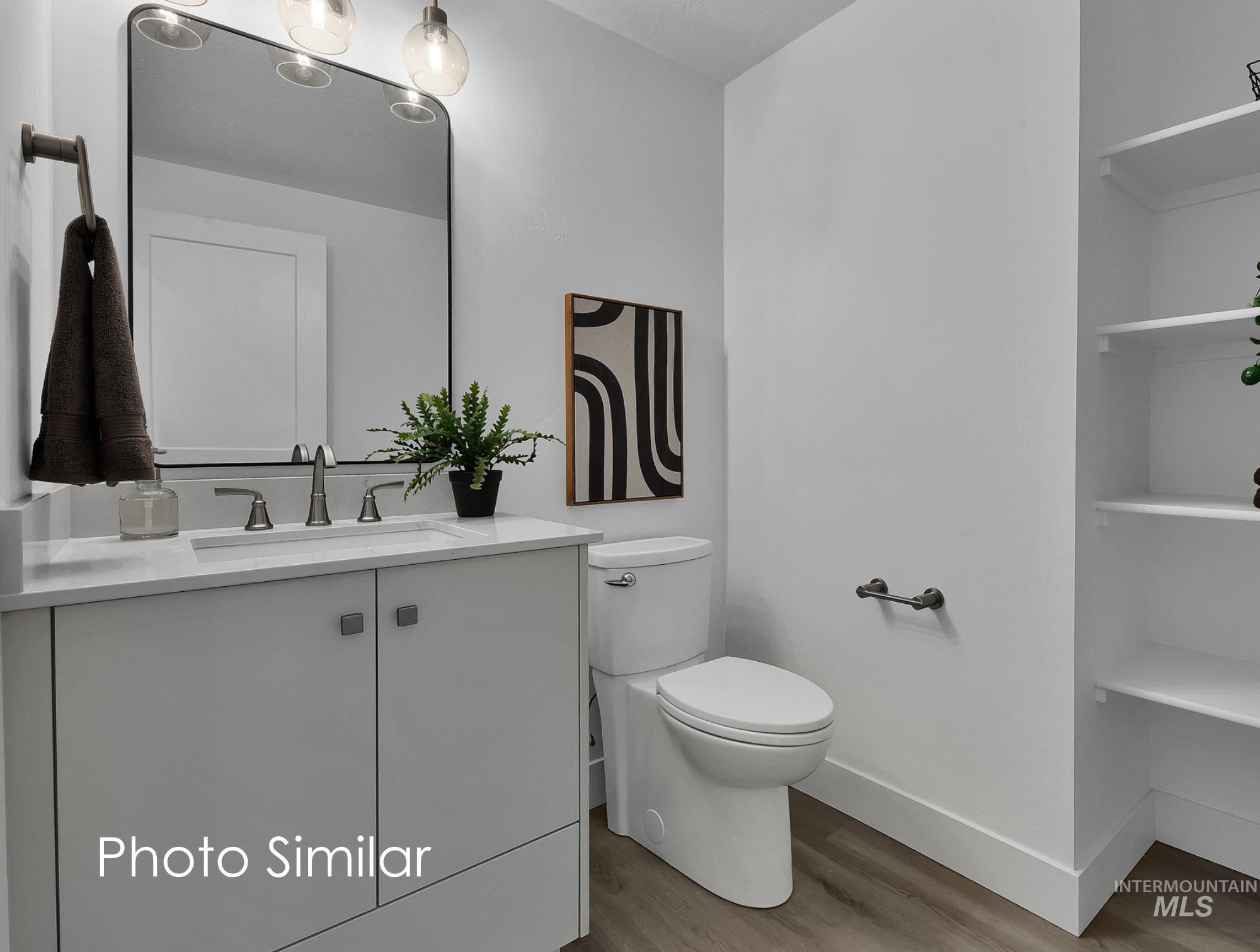 Bathroom featuring a light gray vanity with a white countertop and integrated sink, a rectangular mirror with rounded corners, a two-piece toilet, and built-in shelving