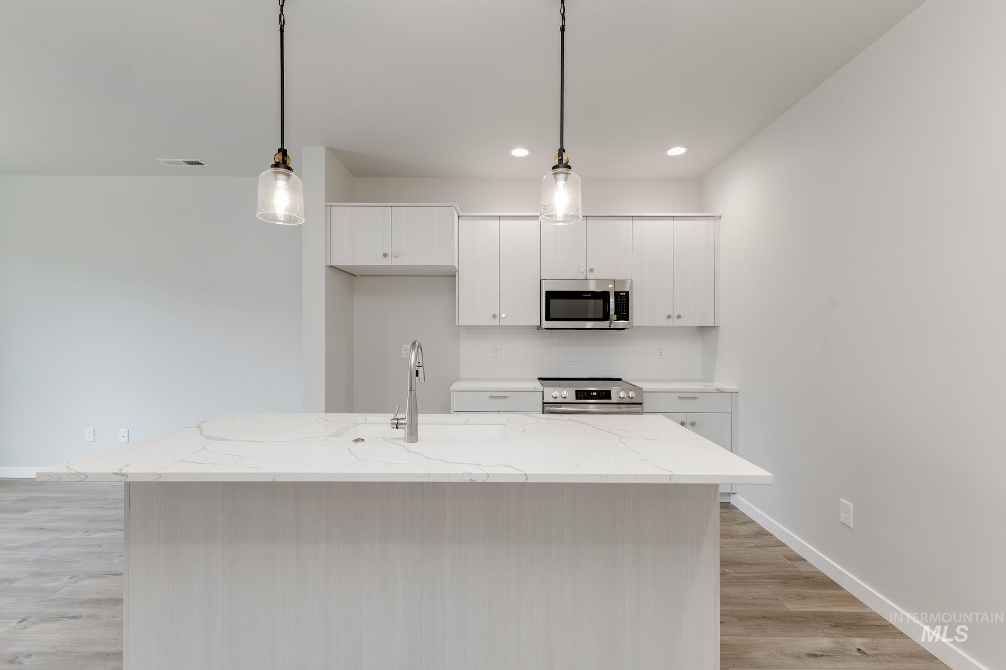 Kitchen with light stone countertops, appliances with stainless steel finishes, hanging light fixtures, a kitchen island with sink, and white cabinets