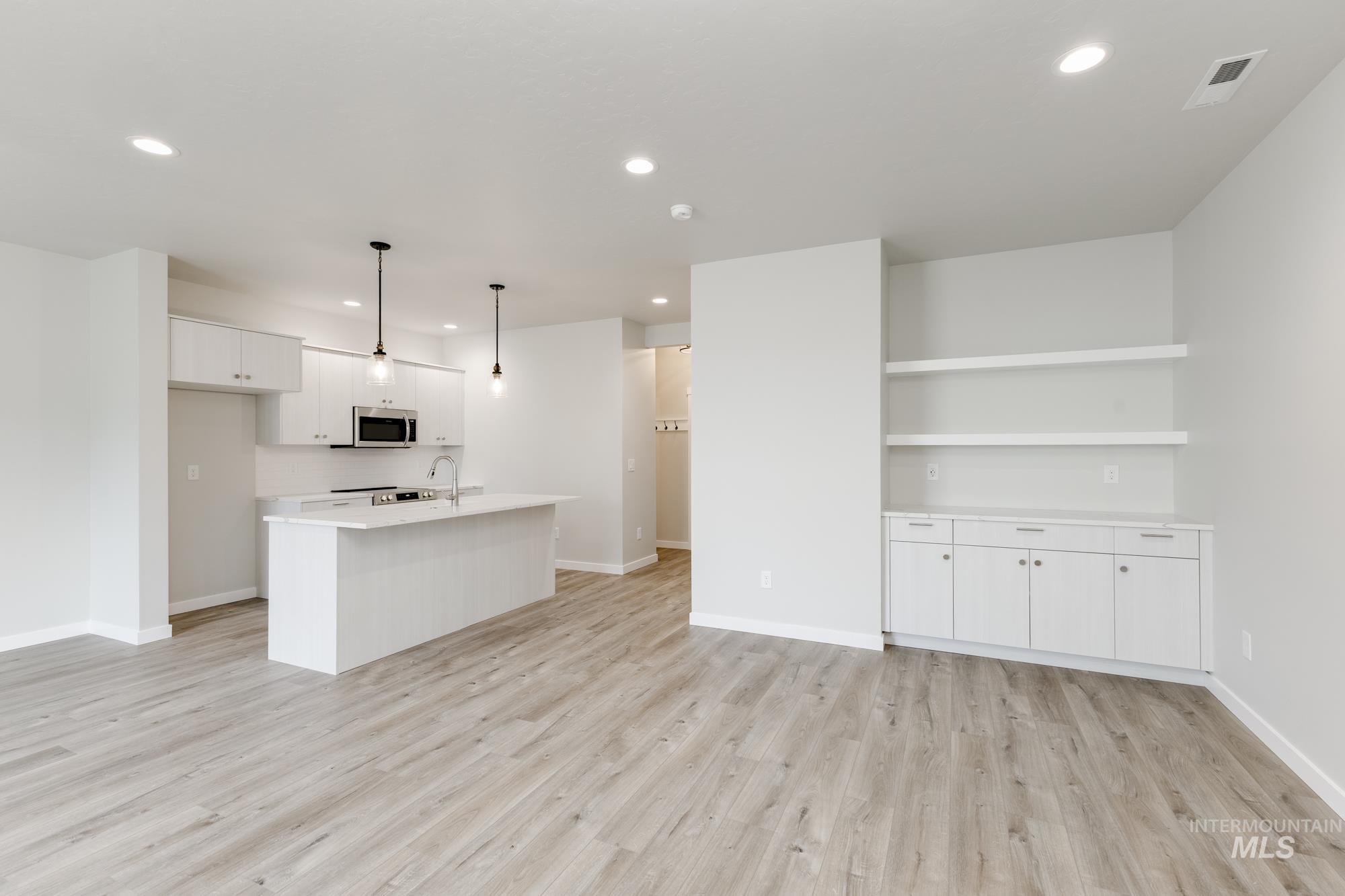 Kitchen featuring white cabinets, light wood-type flooring, pendant lighting, a kitchen island with sink, and recessed lighting