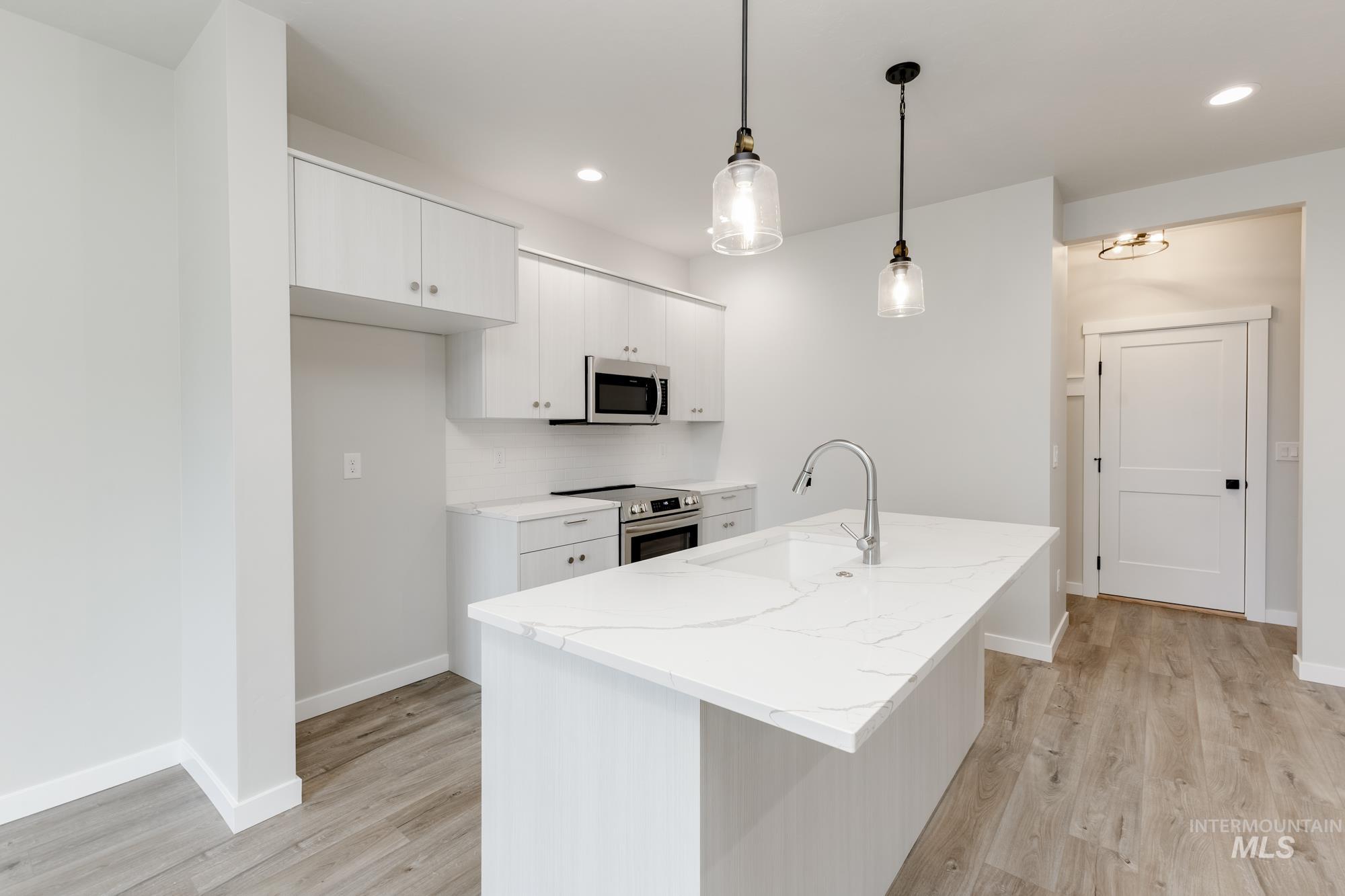Kitchen featuring white cabinets, decorative light fixtures, stainless steel appliances, light wood-style floors, and a kitchen island with sink
