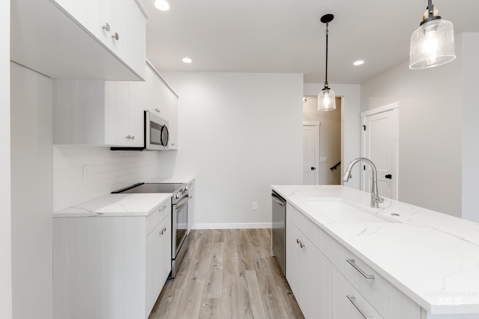 Kitchen with white cabinetry, stainless steel appliances, light stone counters, hanging light fixtures, and light wood-style floors