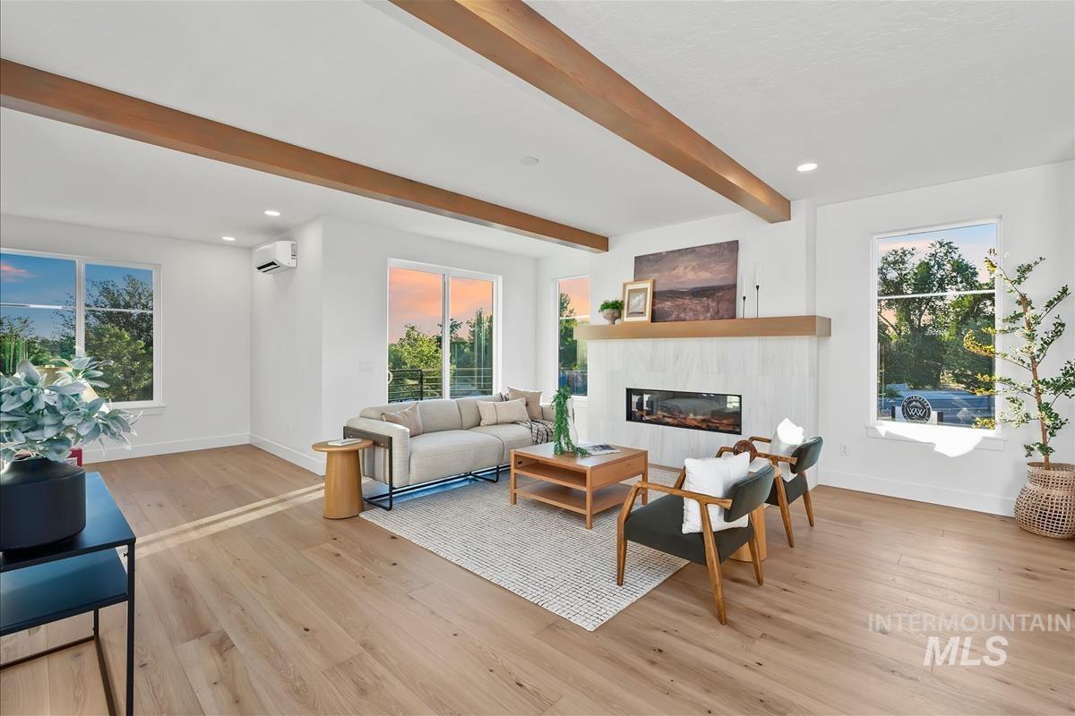 Spacious living area featuring exposed wood beams, wood-finish flooring, a contemporary fireplace with a stone surround, and multiple windows