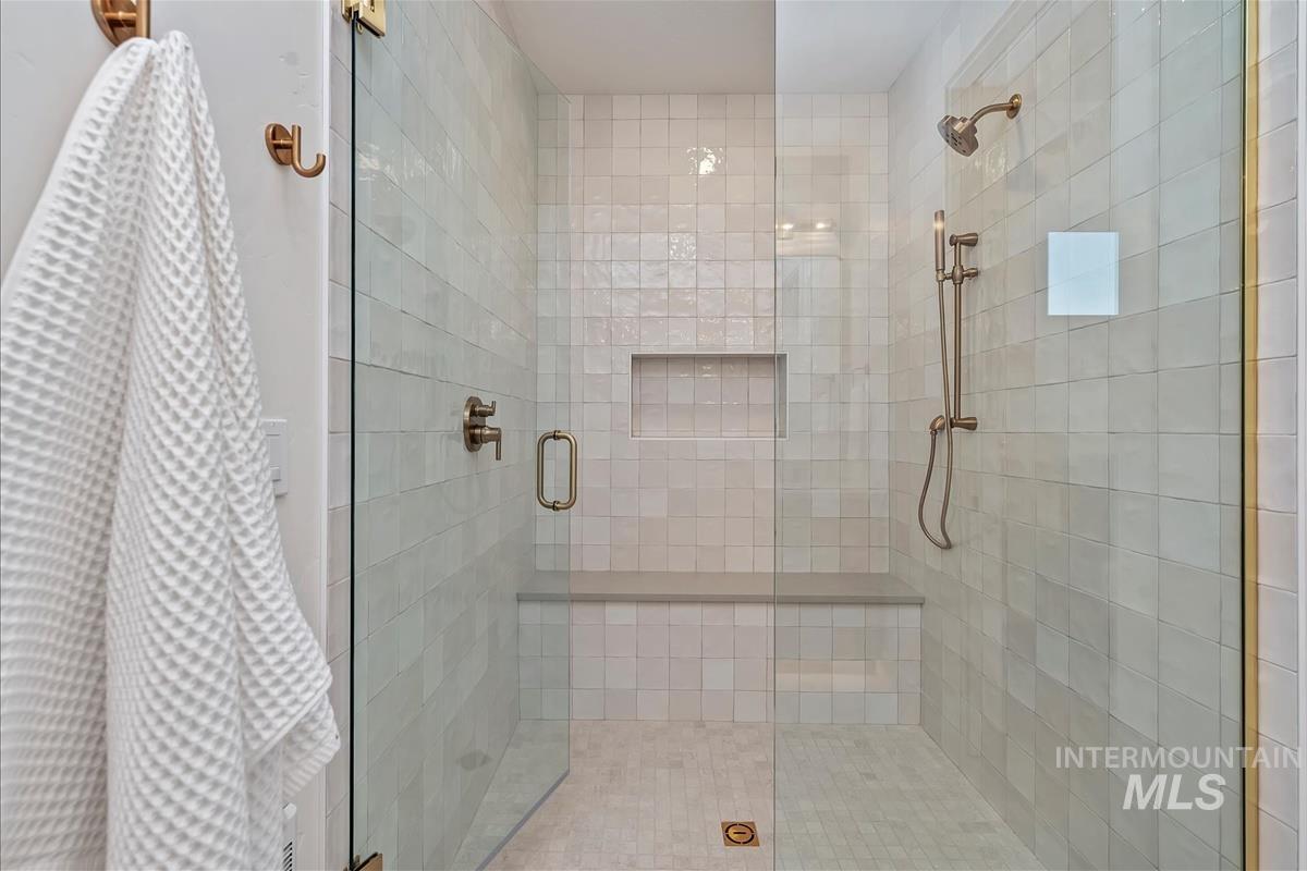 Walk-in shower featuring clear glass enclosure with bronze hardware, tiled walls, built-in bench, recessed shelf, and bronze shower fixtures including a handheld showerhead